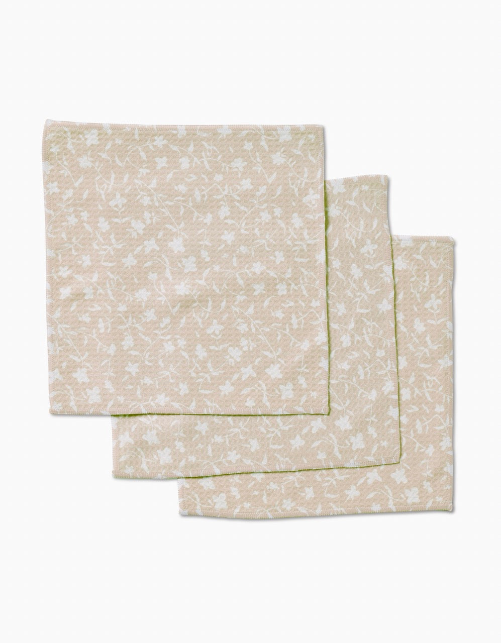 Three beige Tiny Floral cloth napkins by Aubrey Fairchild, featuring a subtle white floral pattern and crafted with ultra-absorbent Geoweave technology, are neatly stacked on a plain white background.