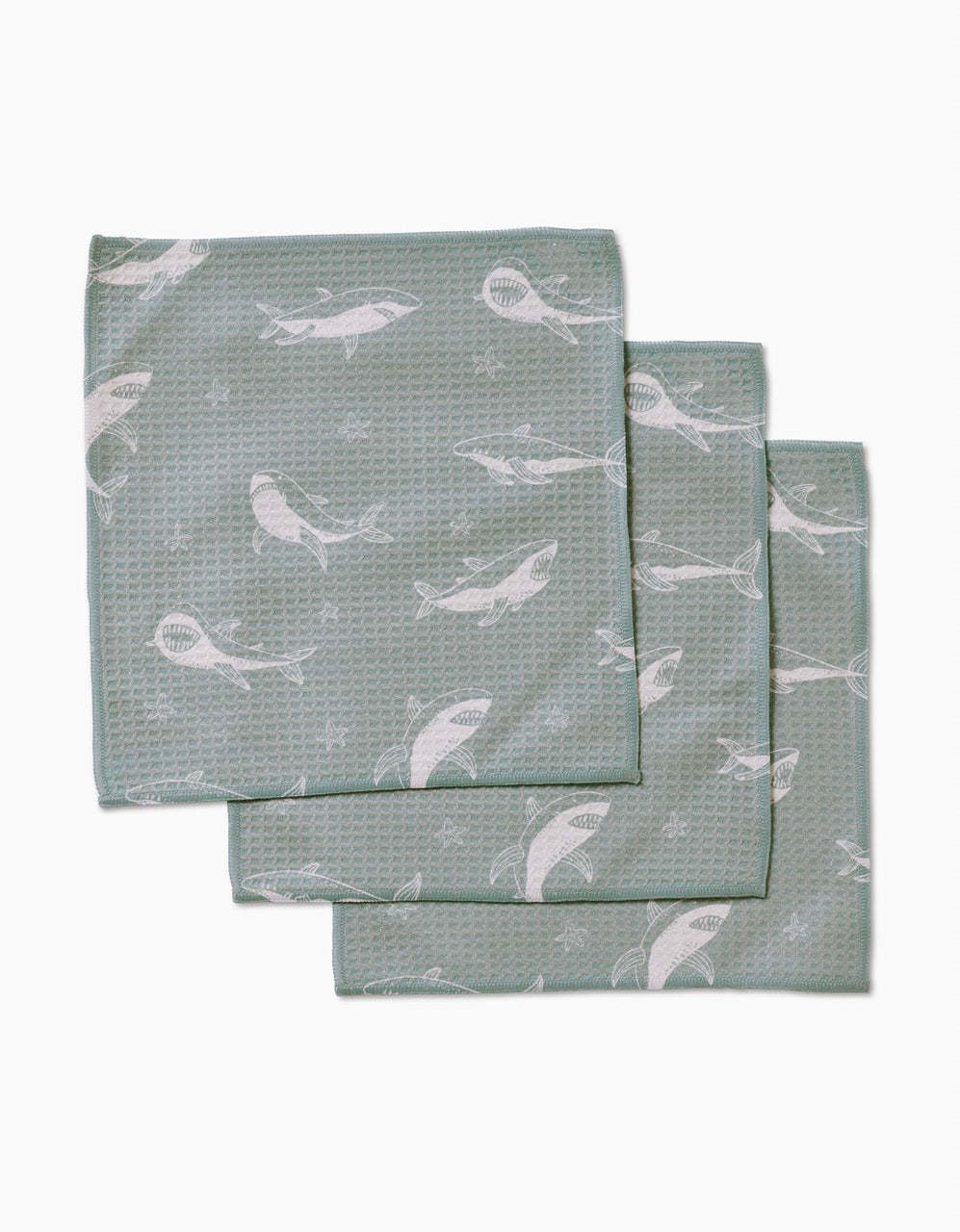 Three folded Toothy Tales washcloths by Janna Sue Design, in green with a textured surface and white whale pattern, are stacked with slight overlap on a plain white background. Made from recycled materials, theyre ultra-absorbent and eco-friendly.