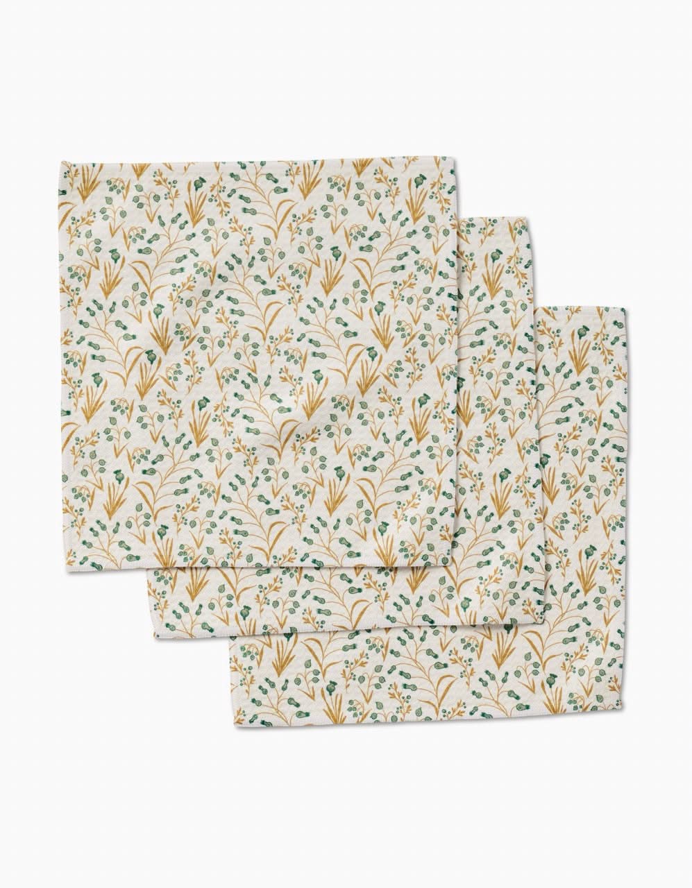 The Wildlight napkins by Danelys Sidron are three neatly stacked, square cloth napkins made from recycled materials, featuring a delicate green leaf and yellow flower botanical pattern on a light background.