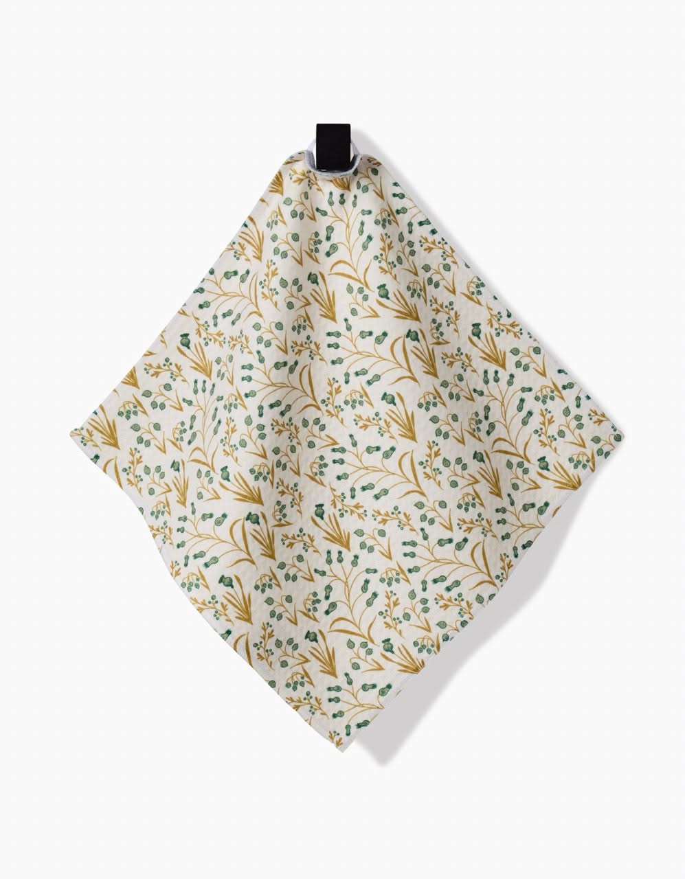 The Wildlight napkin by Danelys Sidron is cream-colored, made from recycled materials, and features a small green, yellow, and blue floral pattern. It hangs from a black loop against a white background.
