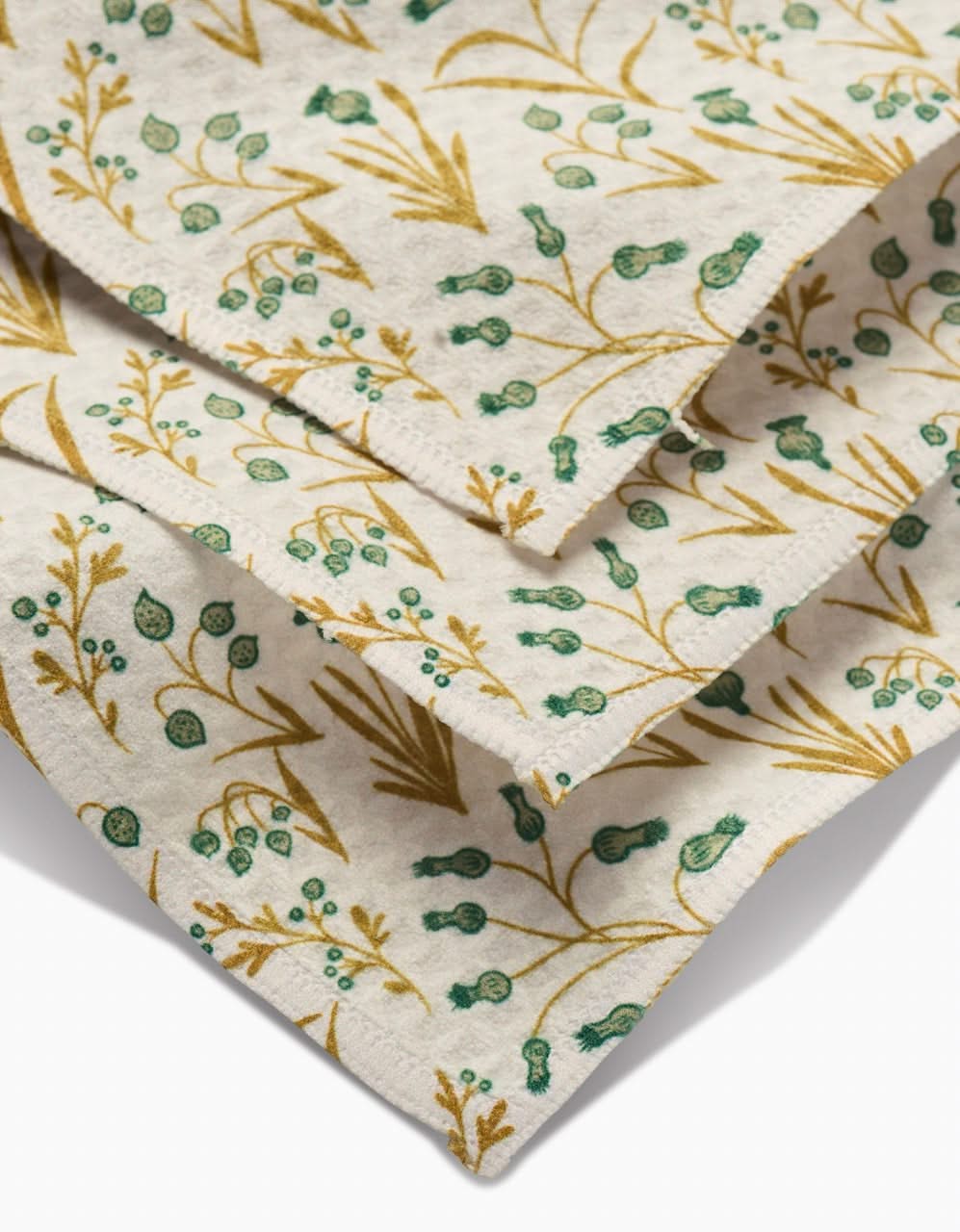 Close-up of Wildlight fabric napkins by Danelys Sidron, featuring green and yellow botanical prints on beige. Ultra-absorbent and elegantly layered, they add a stylish touch to any table setting.