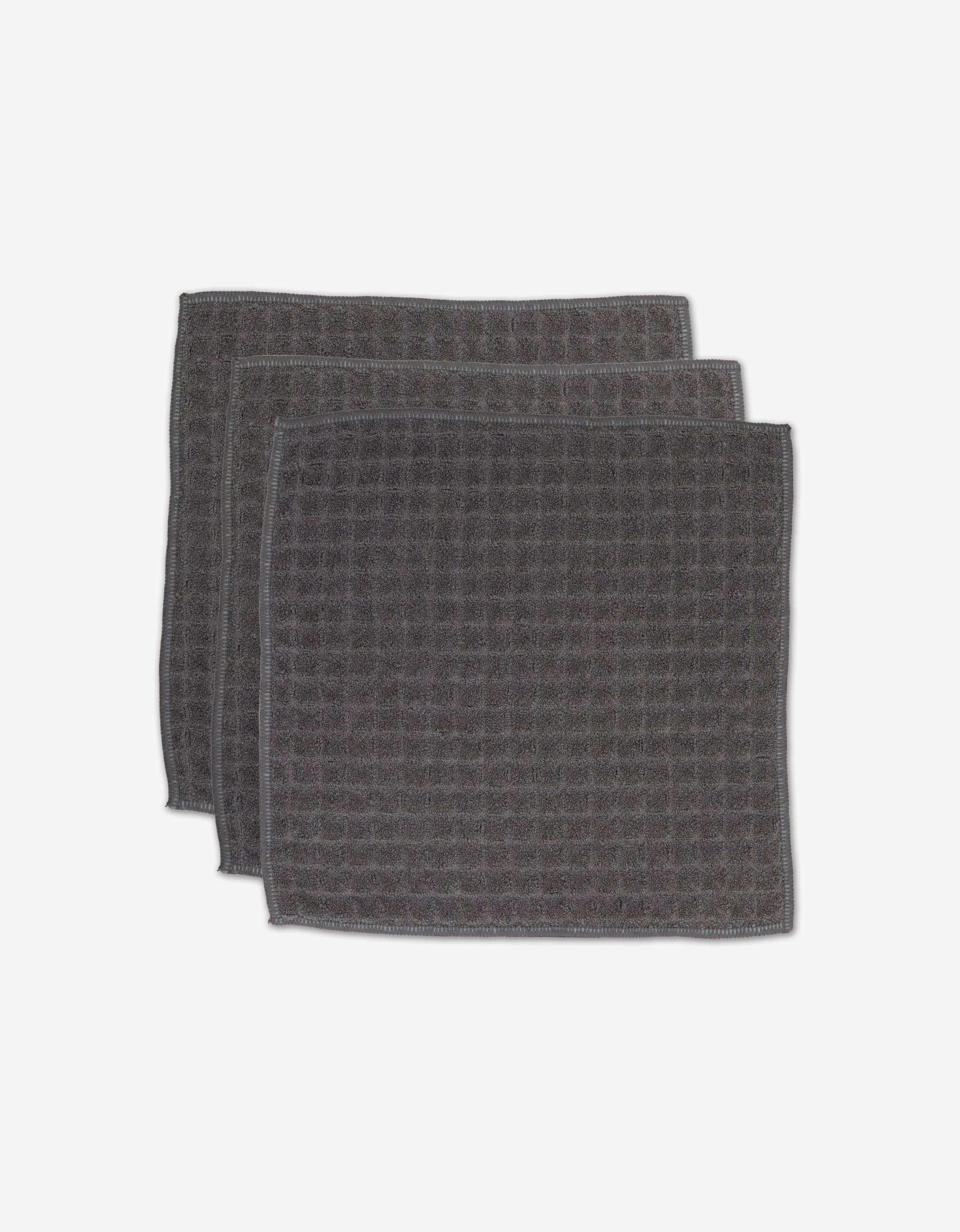 Three GEOMETRY Charcoal washcloths, featuring a dark gray color and square waffle design, are stacked with slight overlap on a white background.