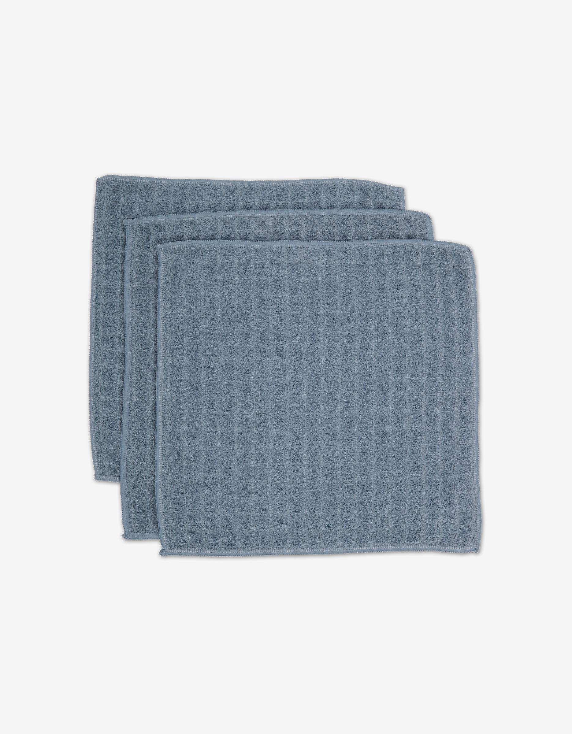 Three Sky washcloths by GEOMETRY, featuring a blue waffle texture and square shape, are stacked against a white background—an eco-friendly, stylish upgrade to your daily routine.