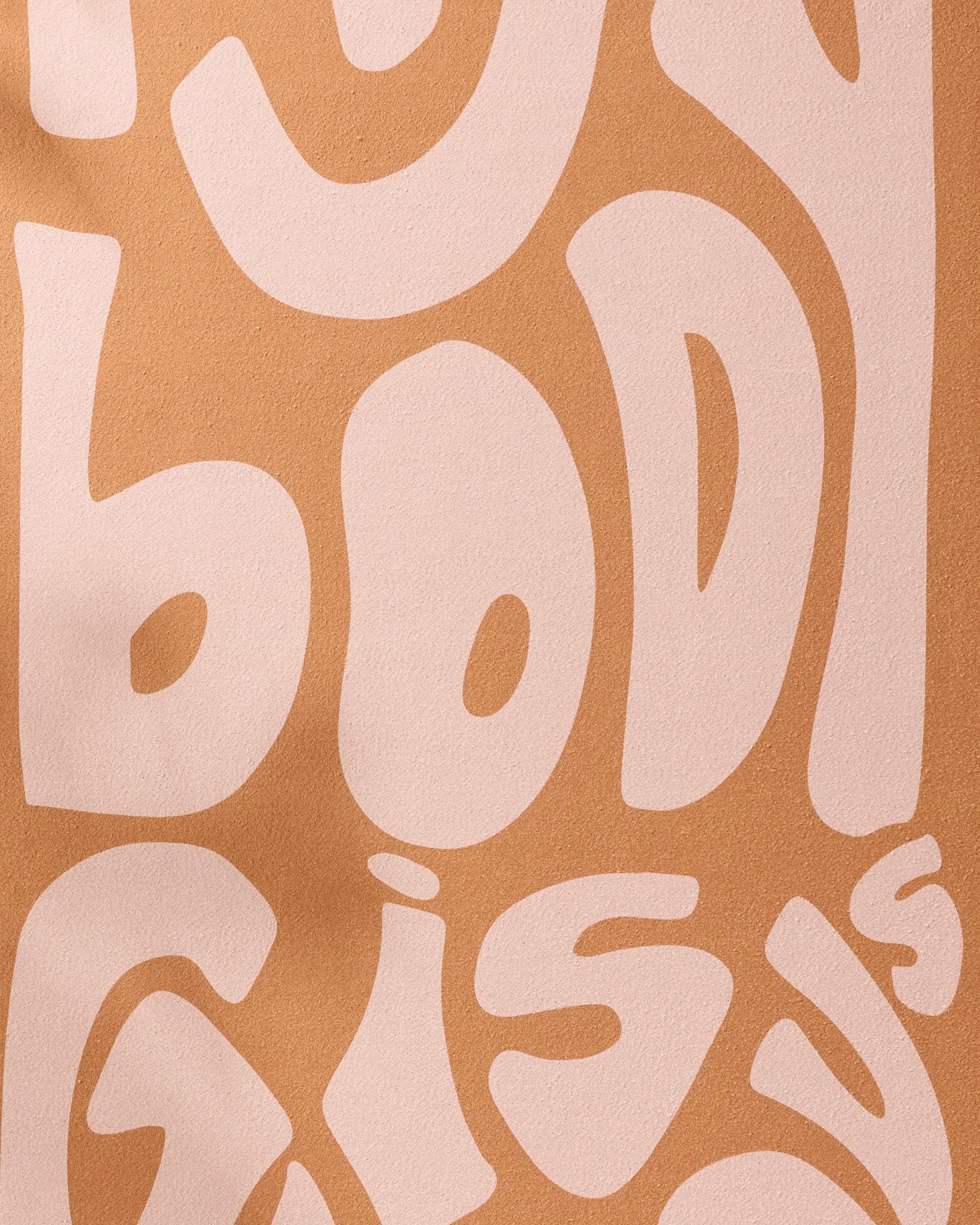 Large, wavy, cream-colored letters on a light brown background spell "body," evoking the comfort and support of the Glorious non-slip yoga towel by Arielle Estoria; some words are partially cut off at the top and bottom.