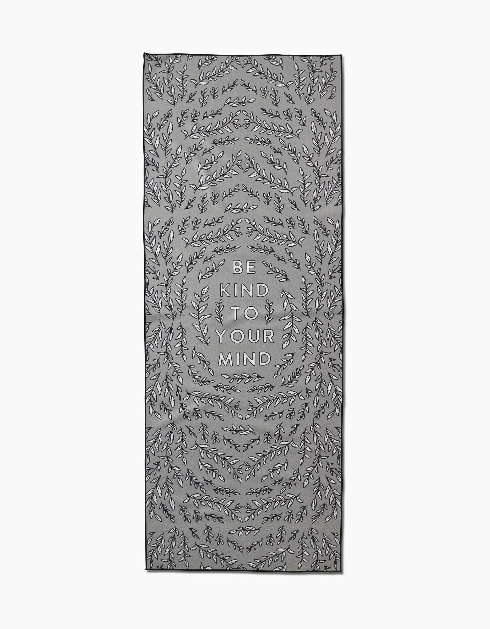 The Graphics and Grain Be Kind To Your Mind yoga towel is rectangular, gray, features black leafy vine patterns, is made from recycled materials, and has BE KIND TO YOUR MIND printed in uppercase at the center.