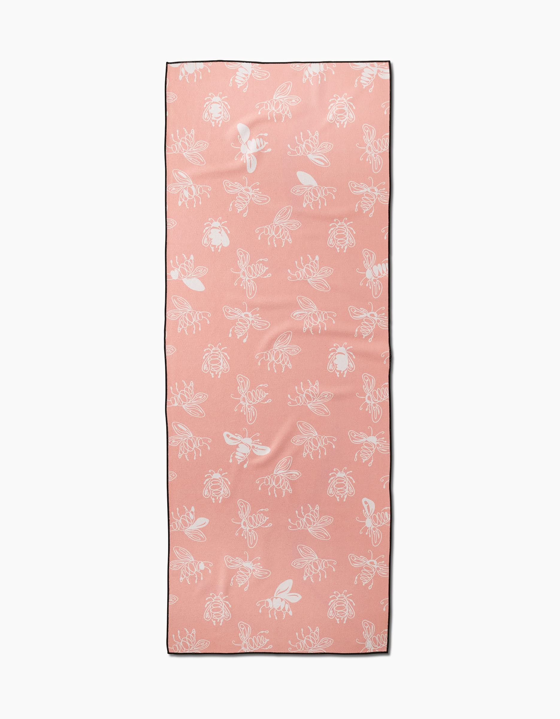 The Sara Mari Beelieve yoga towel is rectangular, peach-colored, and slip-resistant, featuring white minimalist line drawings of bees and flowers in a repeating pattern.