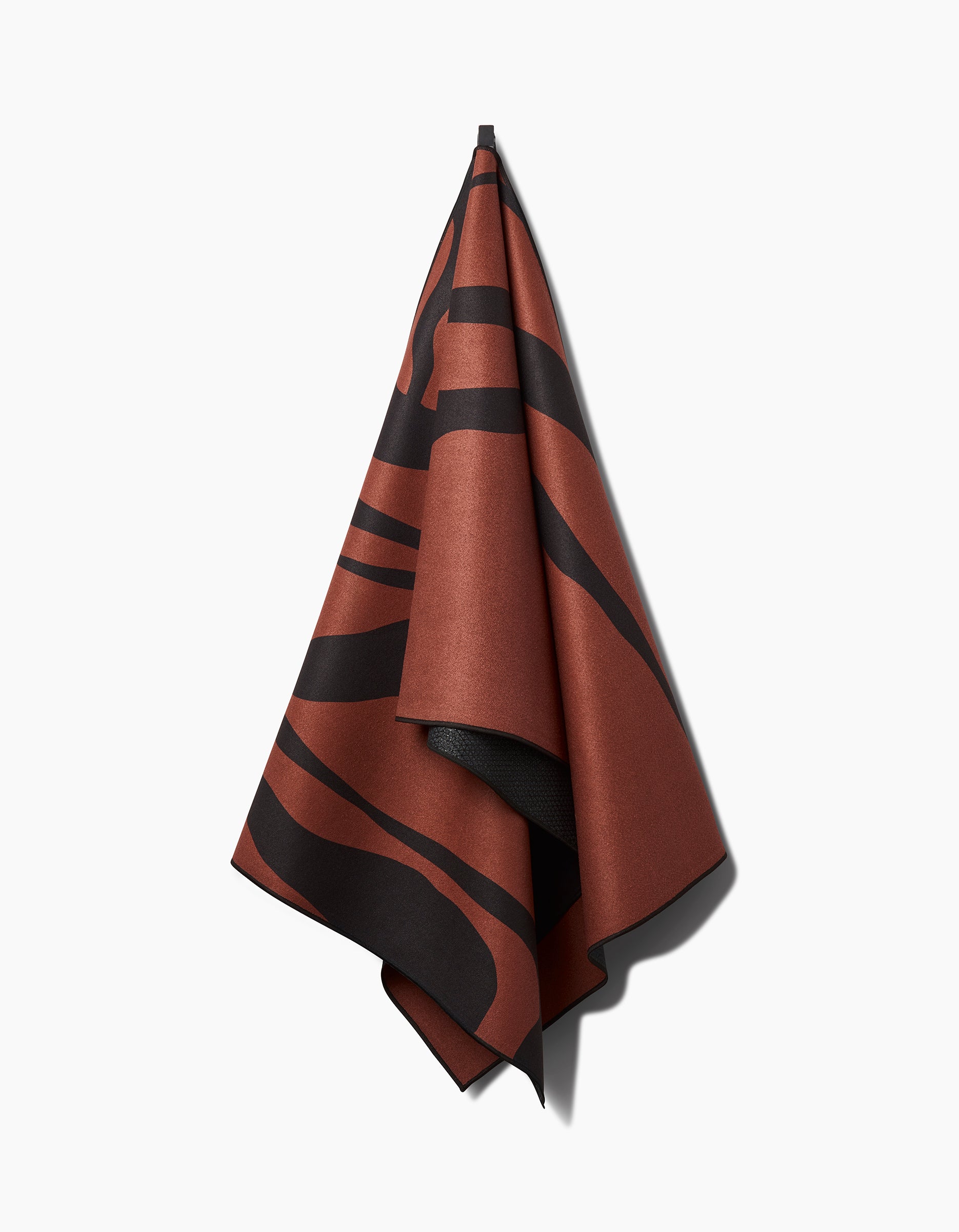 The Cole Strem Black Swirl yoga towel, featuring a brown and black abstract pattern, hangs from a single point against a white background, its folds casting soft shadows.