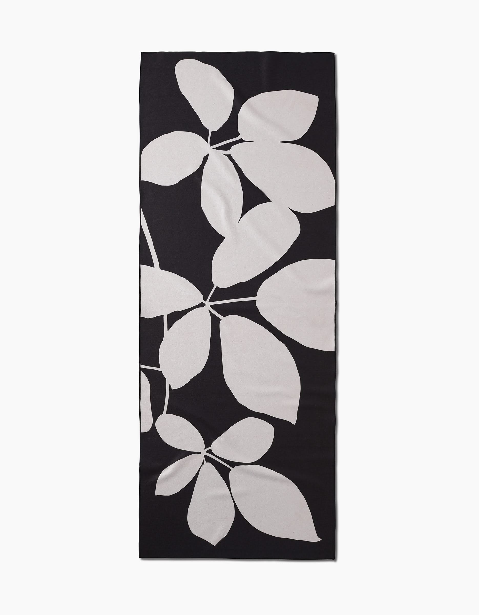 The Blackberry by PrintedPlant is a rectangular black yoga mat featuring a large white leaf design, made from recycled materials for eco-friendly practice.