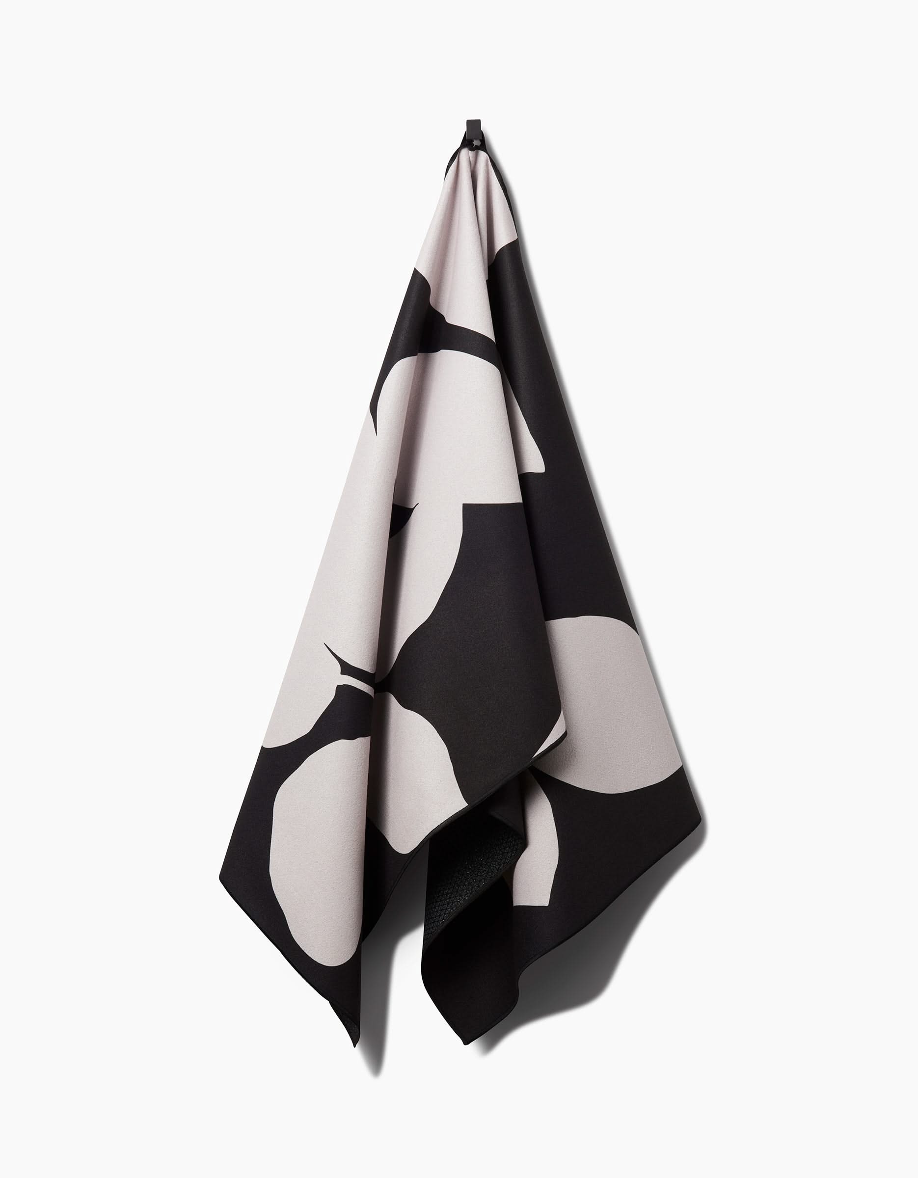 PrintedPlant’s Blackberry yoga towel hangs from a hook against a white backdrop, featuring bold black and white abstract patterns. Made from recycled materials, it brings an eco-friendly touch to your practice.