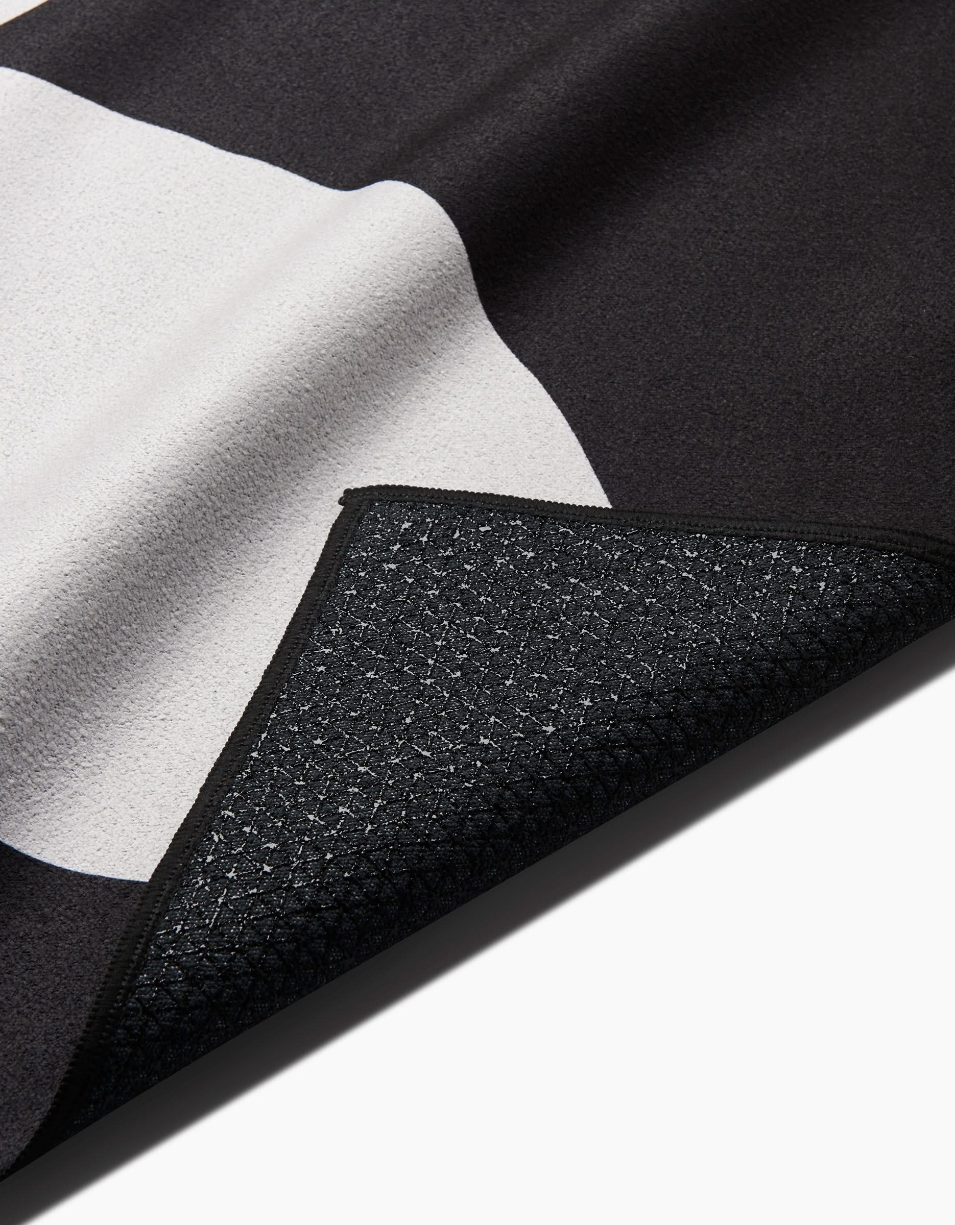 A close-up of the PrintedPlant Blackberry rug features its black and white geometric design with a corner flipped to reveal the textured, non-slip silicone backing.
