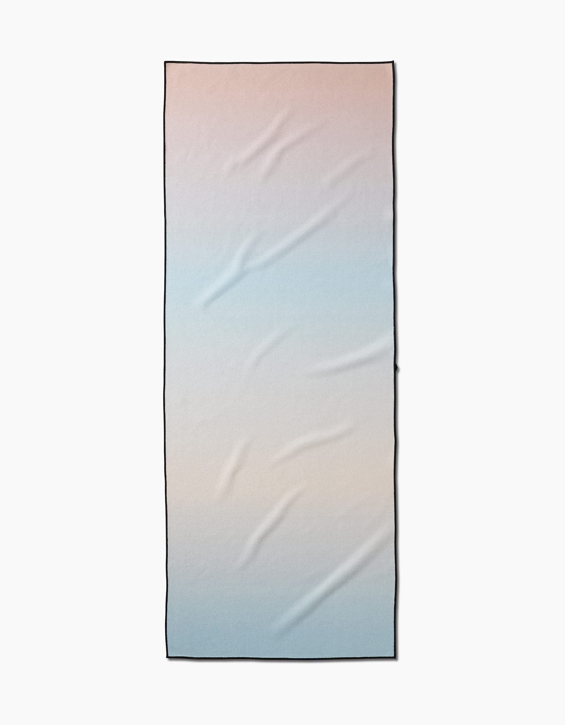 The GEOMETRY Breathe towel is a rectangular recycled yoga towel with a peach-to-light blue gradient, subtle wrinkles, and a thin black border.