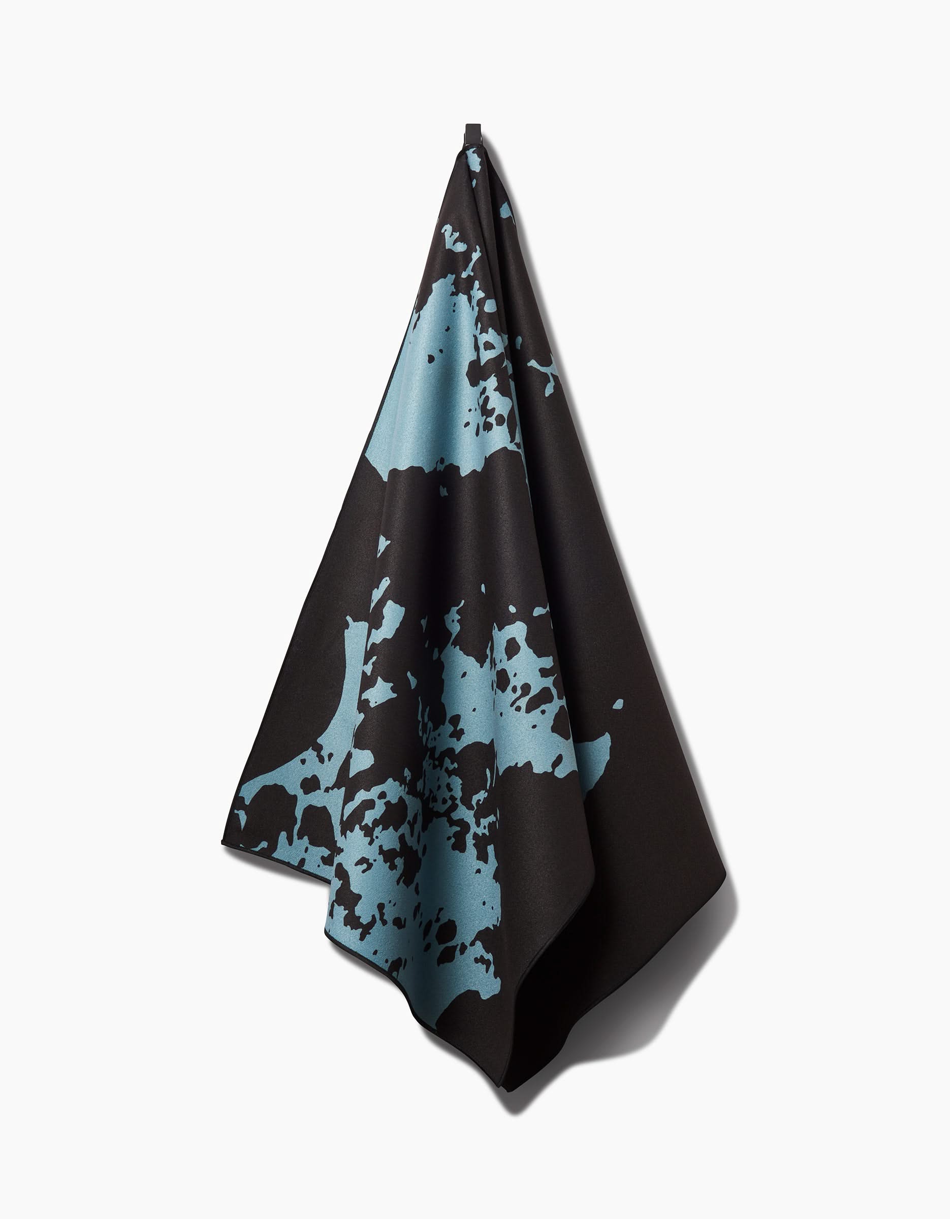 The Cole Strem Brush Stroke yoga towel, crafted from recycled materials, features bold black fabric with large, irregular light blue splatter and hangs from a single point against a plain white background.