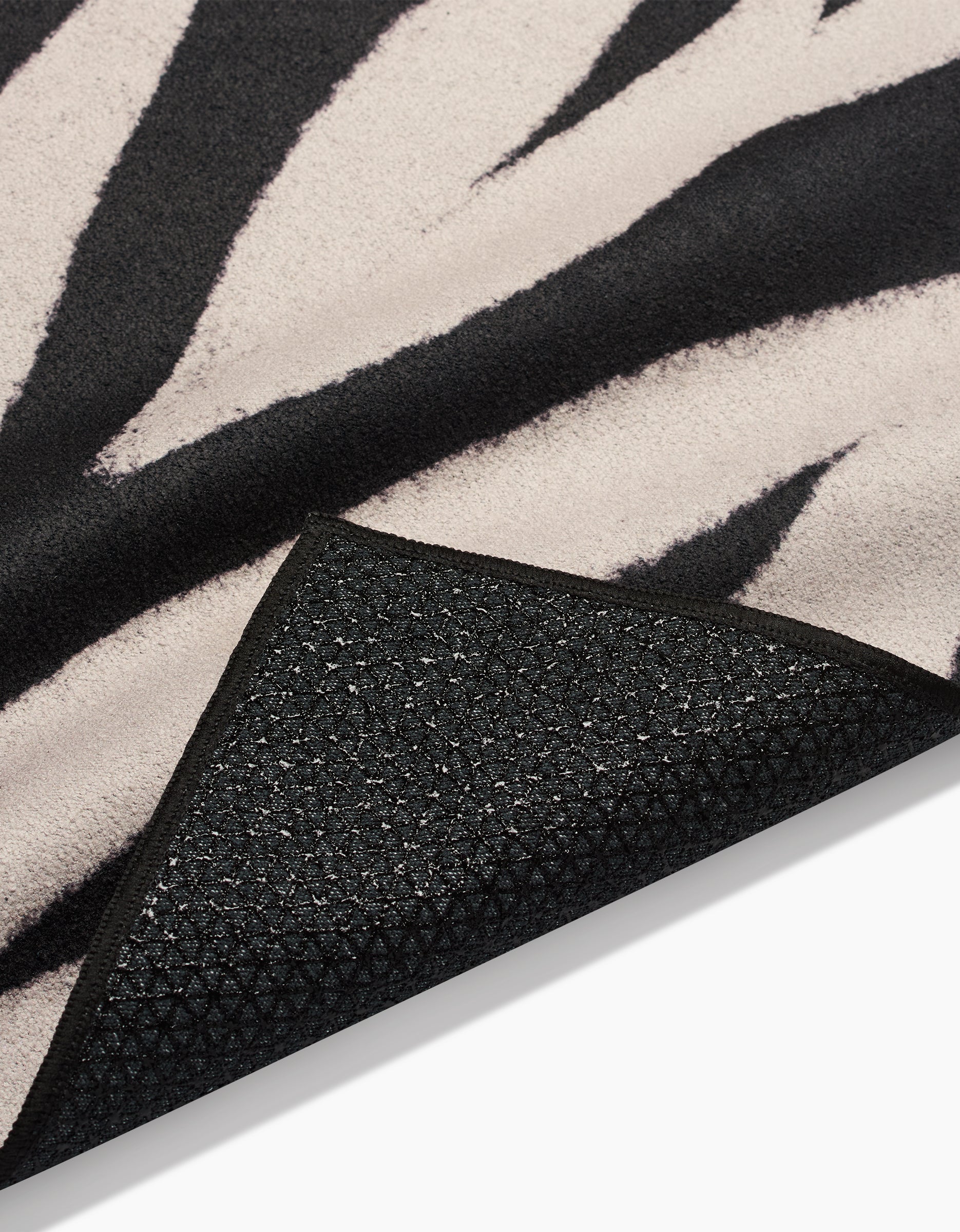 A close-up of the GEOMETRY Chase rug shows its black and white zebra-print stripes and a textured, non-slip Silicone Grip backing at one corner.