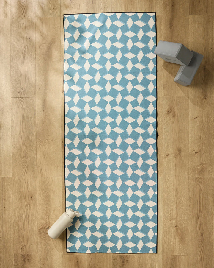 The Geometry Circus Stand Teal Cream yoga mat is laid out on a wooden floor with two gray yoga blocks, a non-slip towel, and a white water bottle nearby.