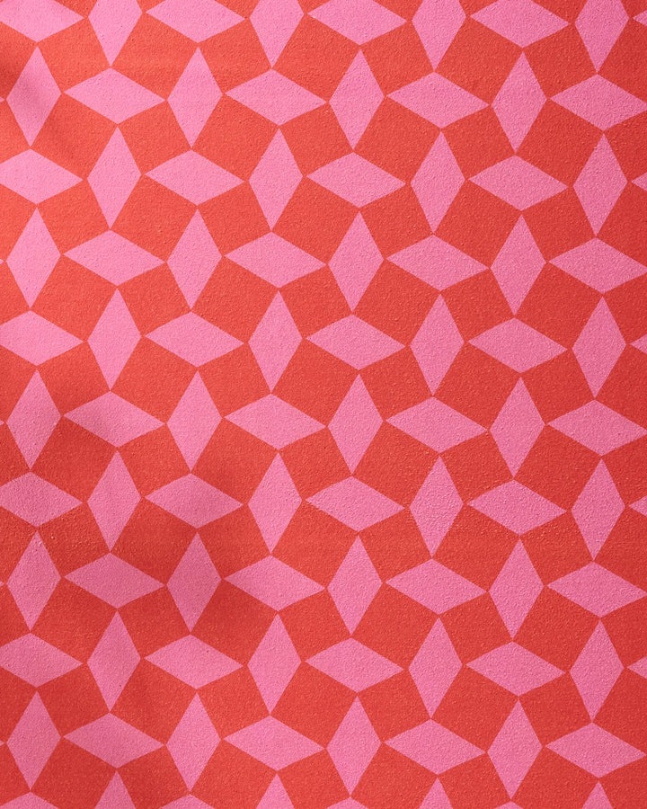 The Geometry Circus Stand Pink Red yoga towel features a pink geometric diamond pattern on red, creating a striking optical illusion with slight folds and shadows that enhance its depth and texture.