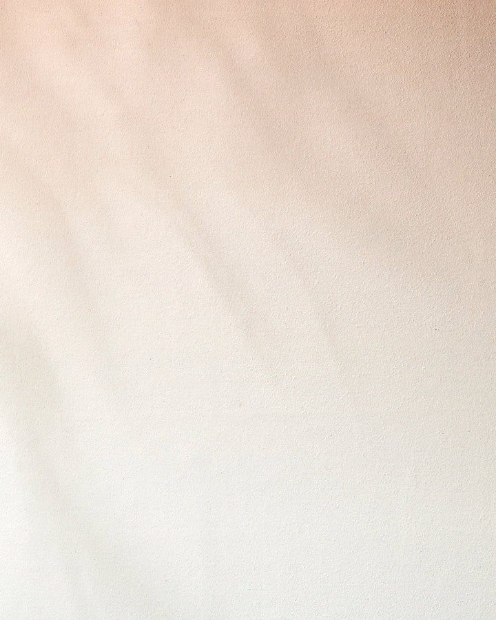 Lightly textured beige wall with soft shadows and a smooth gradient from light tan to off-white, evoking the calming feel of a recycled GEOMETRY Core yoga towel. No distinct patterns or objects visible.