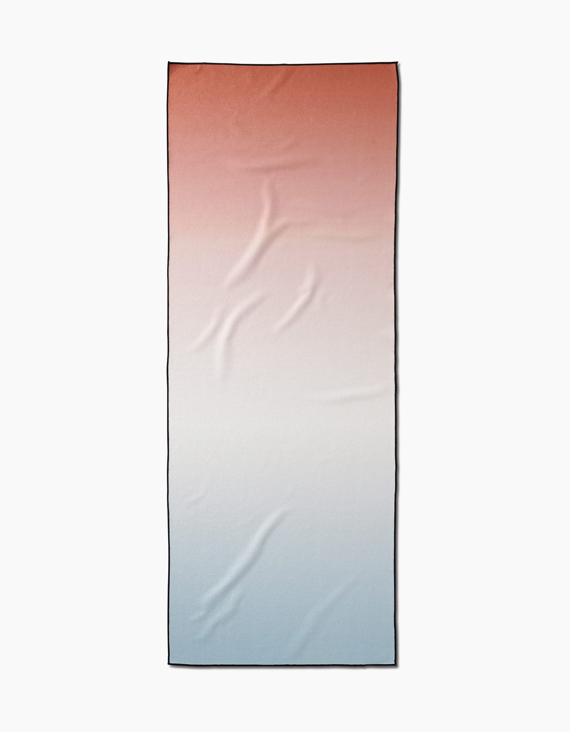 The GEOMETRY Core is a rectangular, slip-resistant yoga towel with a gradient that fades from reddish-brown at the top to white in the middle and pale blue at the bottom, showcasing visible fabric creases.