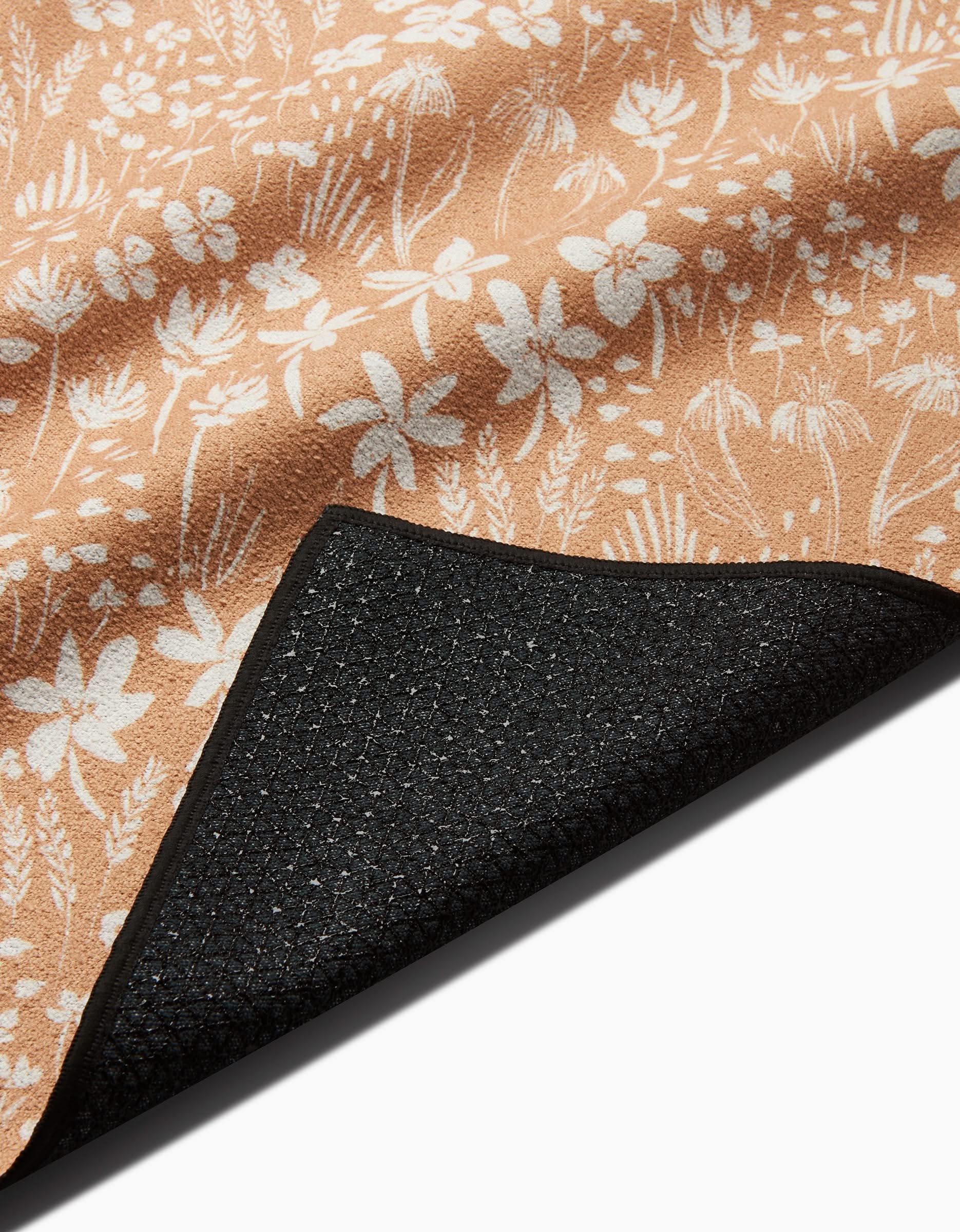 A close-up of the Hufton Studio Floating Meadow mat in tan with a white floral pattern. The corner is flipped to show its textured black, slip-resistant backing.