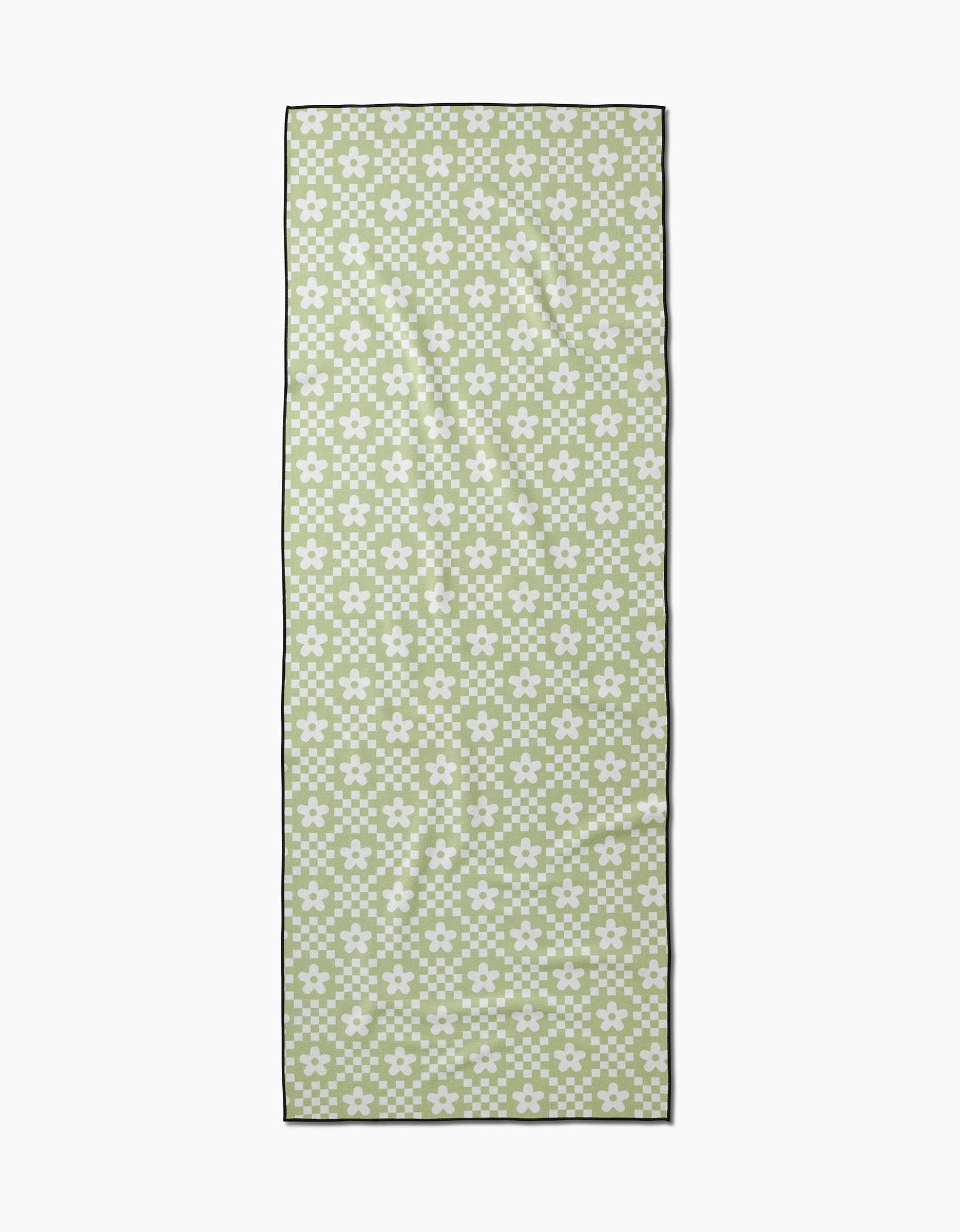 The GEOMETRY Floral Check is a rectangular, recycled yoga towel in green and white, featuring a repeating pattern of small white flowers with green centers outlined in black.