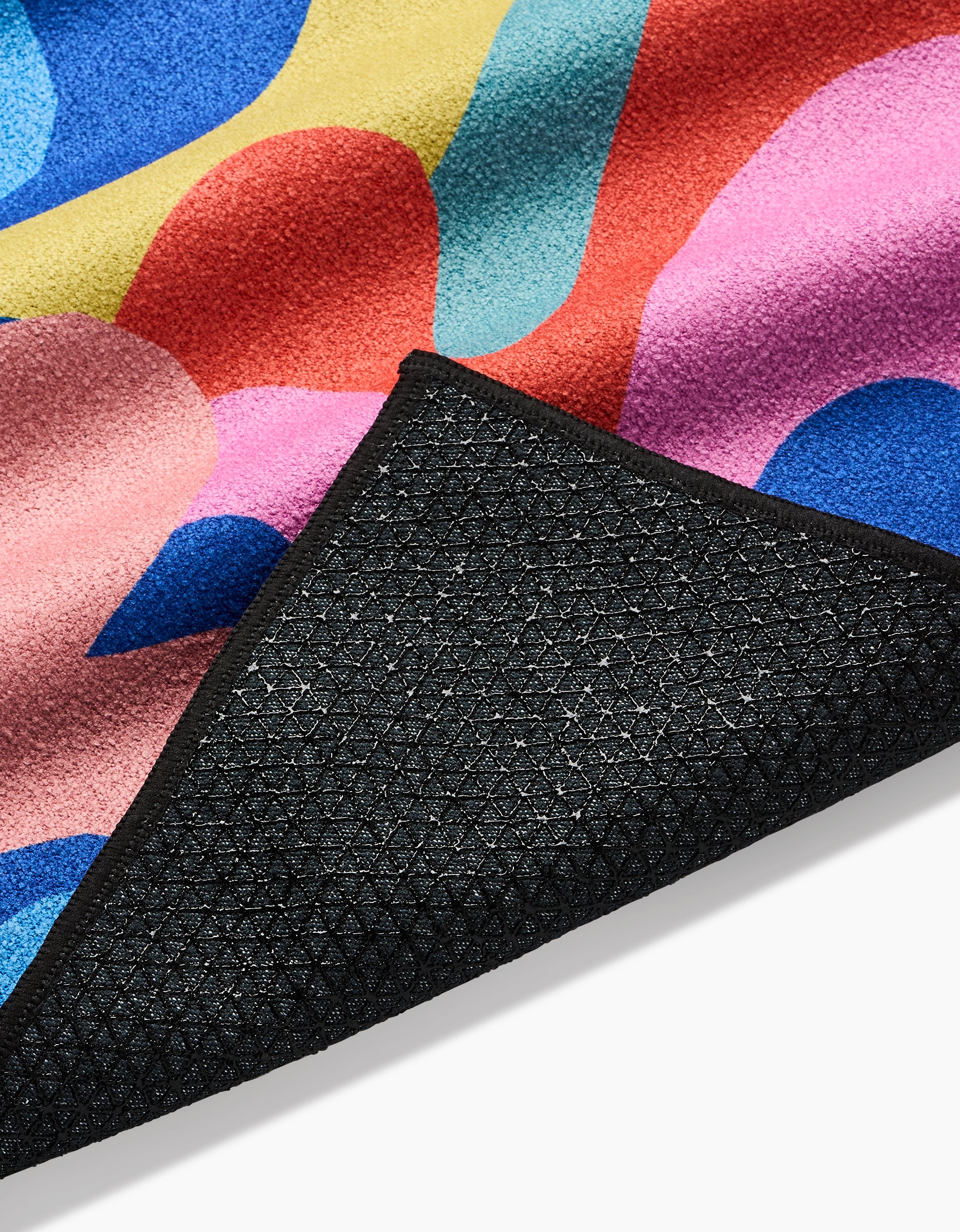 A close-up of the Flower Powers yoga towel by Masha Volnova, featuring a colorful abstract design and a black textured non-slip silicone grip backing, partially folded over.