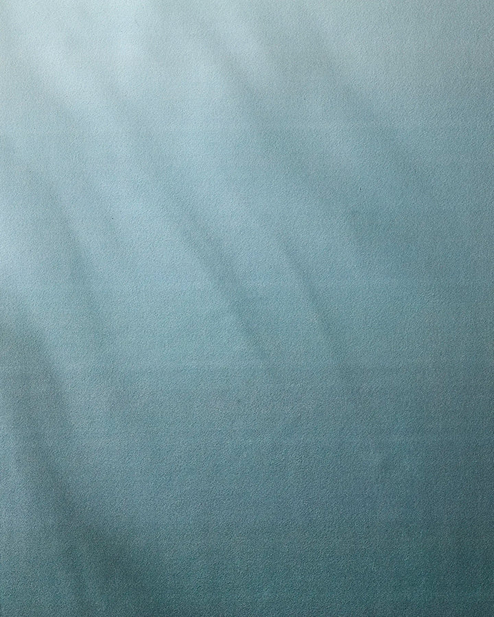 A textured blue surface with soft light and shadow gradients evokes the feel of the GEOMETRY Foundation yoga towel, with faint lines suggesting gentle movement or subtle patterns across the design.