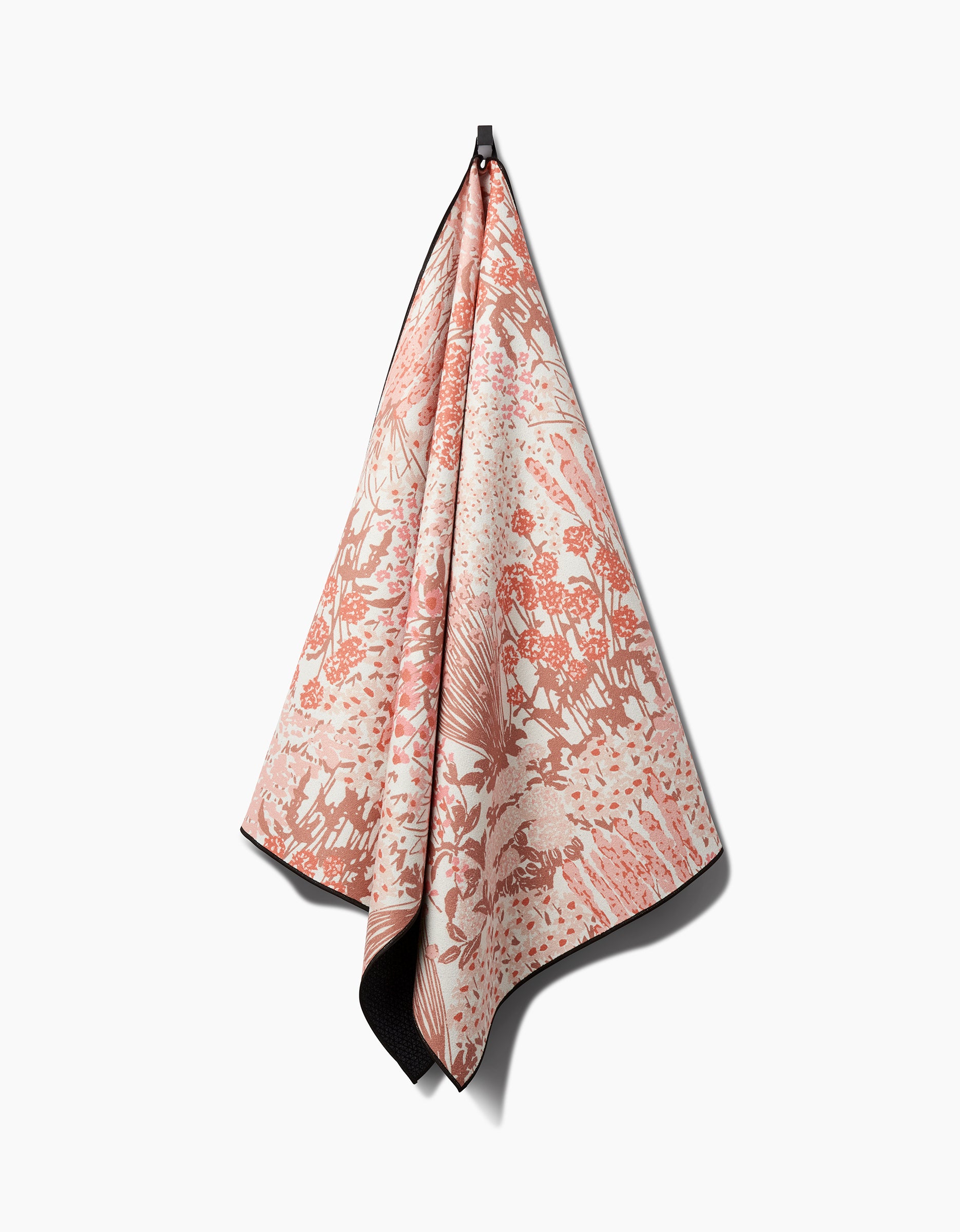 The Hufton Studio Garden Bloom yoga towel, featuring a pink and cream floral botanical pattern, hangs from a hook against a white background. Crafted from recycled materials, its draped folds cast soft shadows to the right.