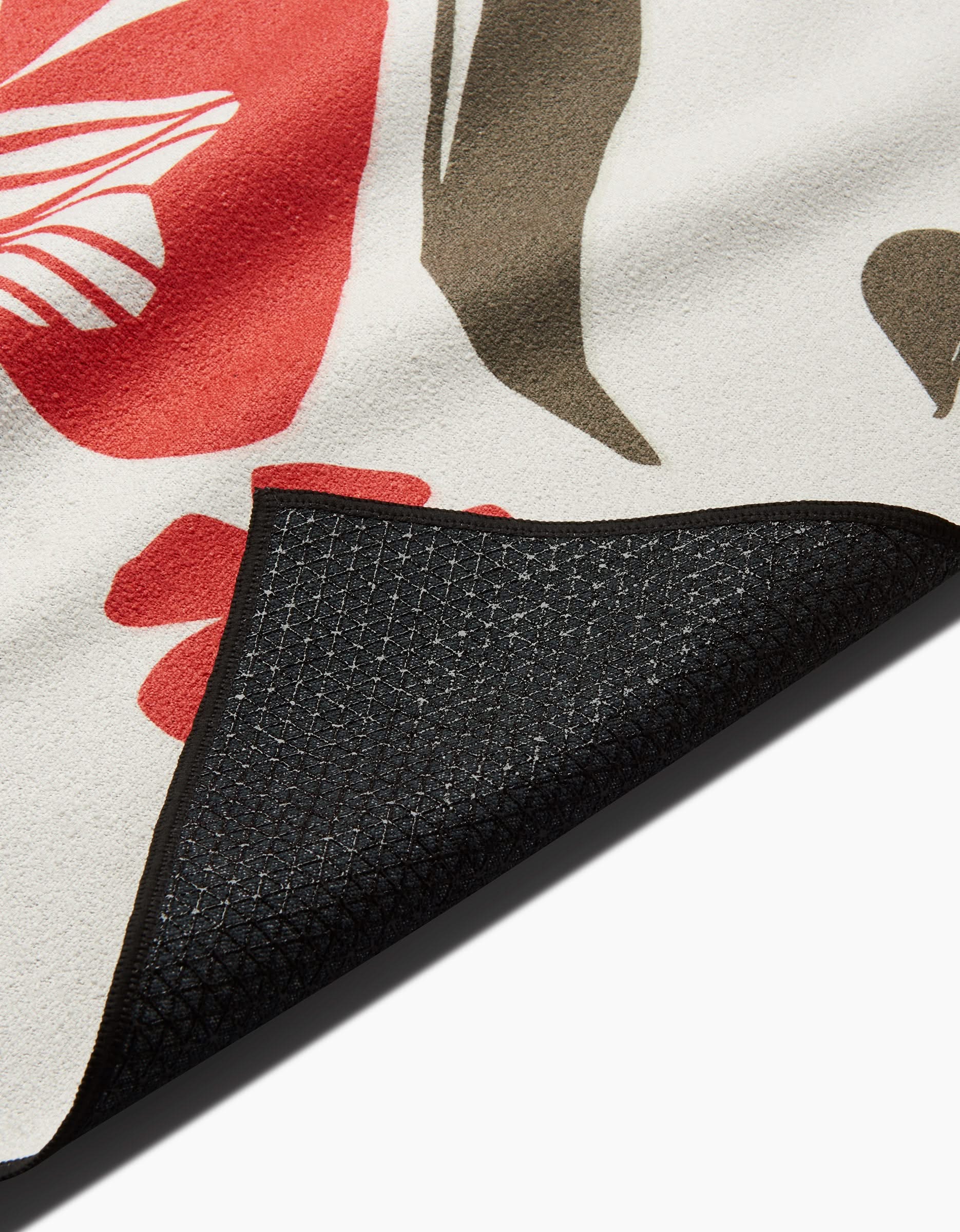 A close-up of the Ash Cascade Garden Stamp mat corner flipped over reveals a black textured silicone grip non-slip underside and a top layer featuring an abstract floral pattern in red, brown, and white.