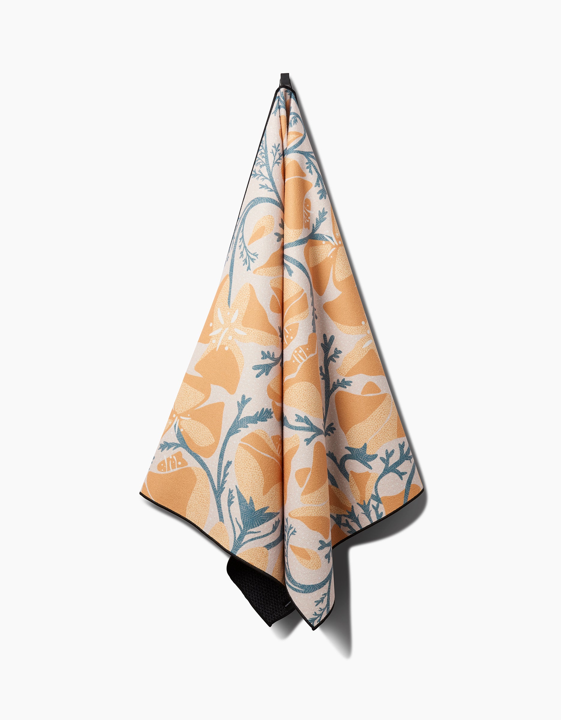 The Julianne Haness Golden Poppy yoga towel, featuring orange and blue floral patterns and slip-resistant design, hangs on a hook against a plain white background.
