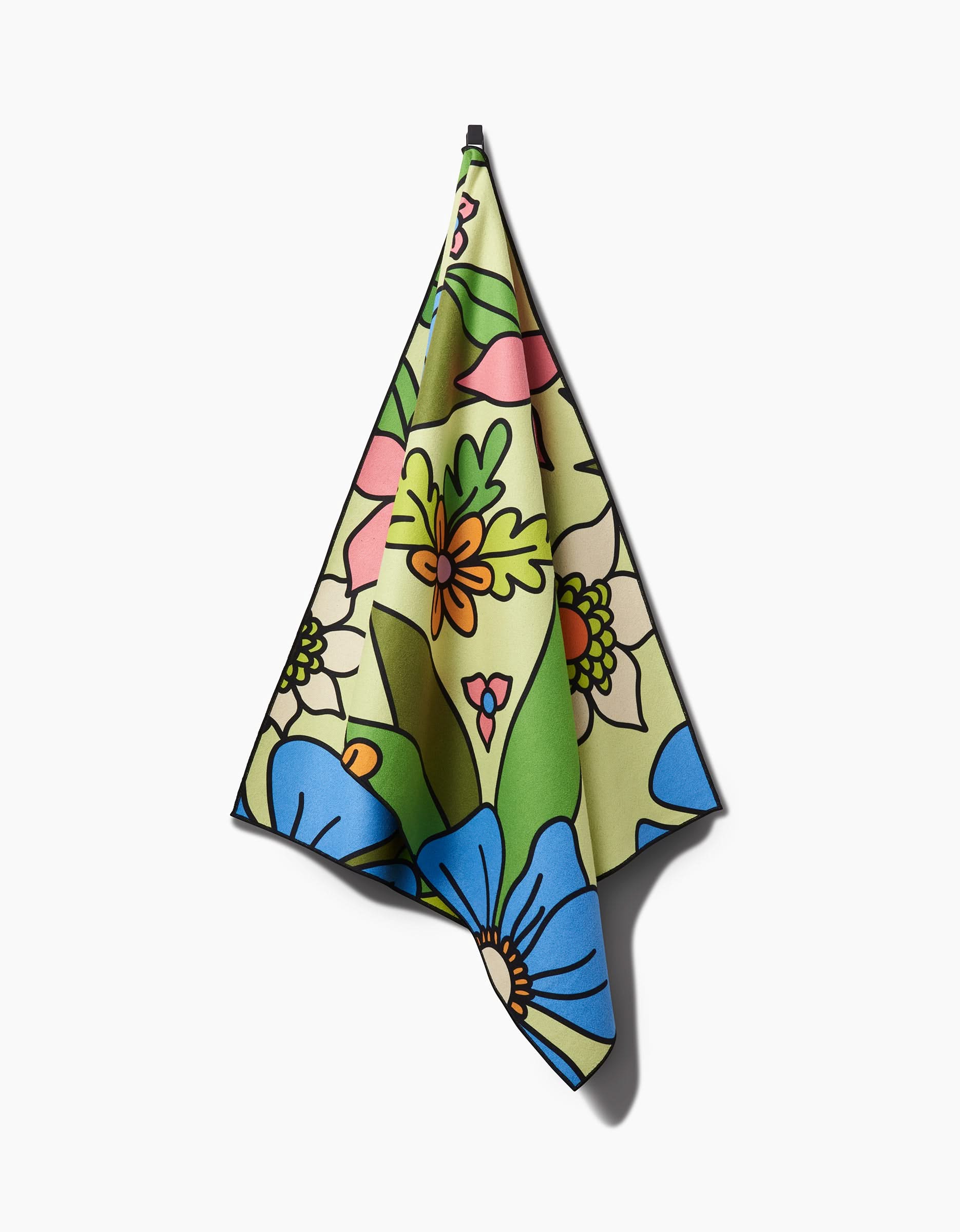 The GEOMETRY Green Flowers yoga towel, featuring a vibrant floral pattern in blue, green, yellow, pink, and orange, hangs against a white background.