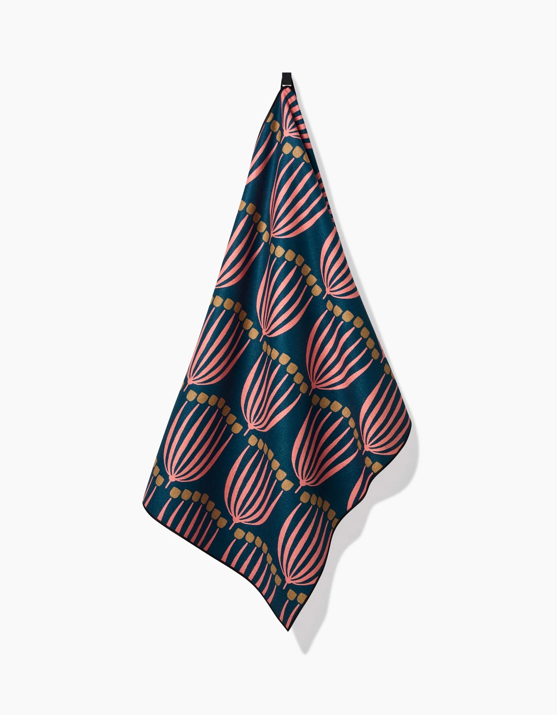 The Josie yoga towel by Amy MacCready, crafted from recycled materials in dark blue with a repeating pink and light brown fan-like pattern, hangs from a single point against a white background.