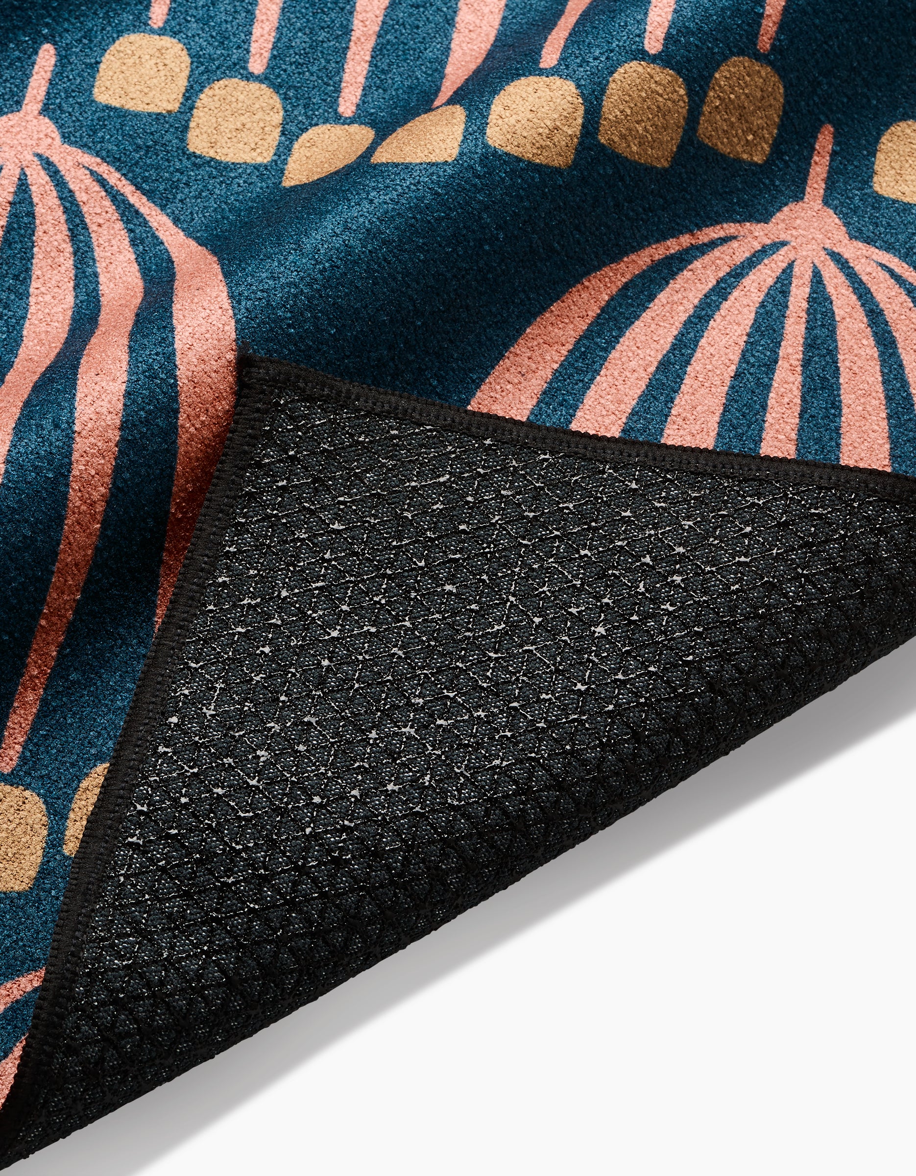 A close-up of the Josie rug by Amy MacCready shows the corner flipped to reveal its slip-resistant black backing. The rug has a blue base with pink and gold abstract shapes and is crafted from recycled materials.