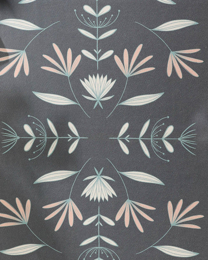 The Jungle Maze yoga towel by Amita Nair features a slip-resistant surface with stylized floral patterns in light pink, white, and pale green on a geometric dark gray background.
