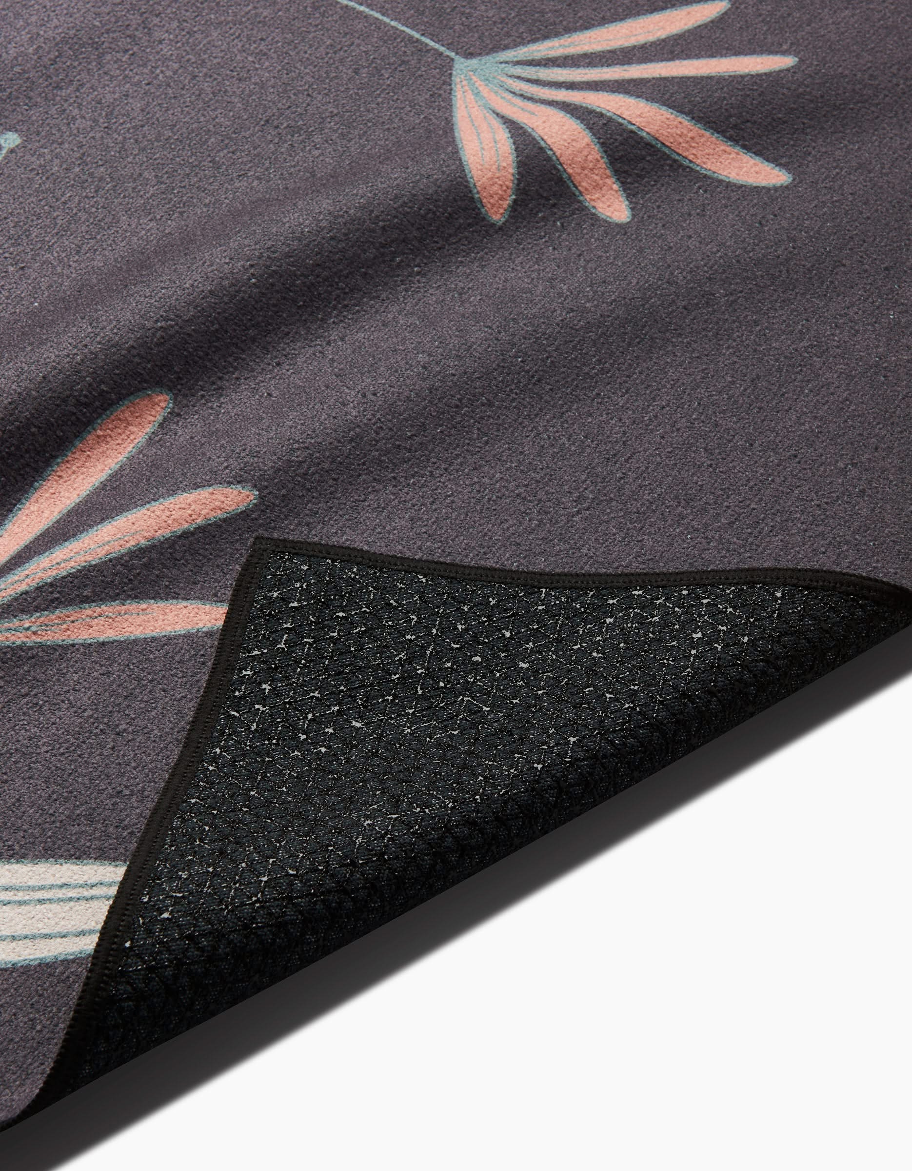 A close-up of Amita Nairs Jungle Maze rug shows dark hues with pink and light blue floral patterns, plus a textured non-slip black backing at the corner made from recycled materials.