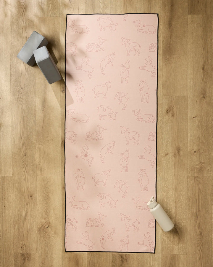 The Sara Mari Kidding Around pink yoga mat with animal line drawings is spread on a wooden floor, topped with a non-slip towel. Two gray yoga blocks and a white water bottle are placed next to the mat.