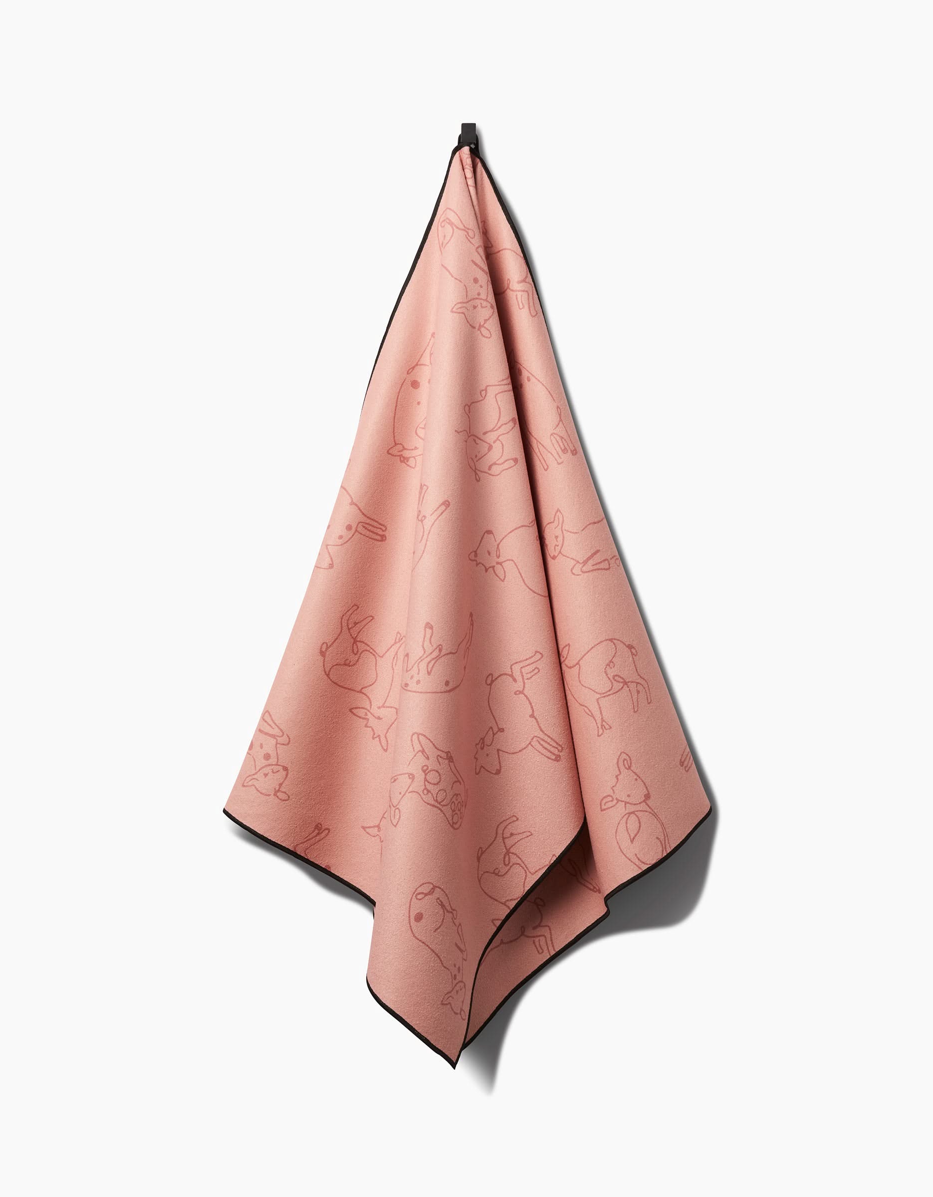 The Sara Mari Kidding Around yoga towel in pink features black edges and slip-resistant backing, adorned with black line drawings of various dogs. It hangs on a hook against a white background, displaying a soft, draped look.