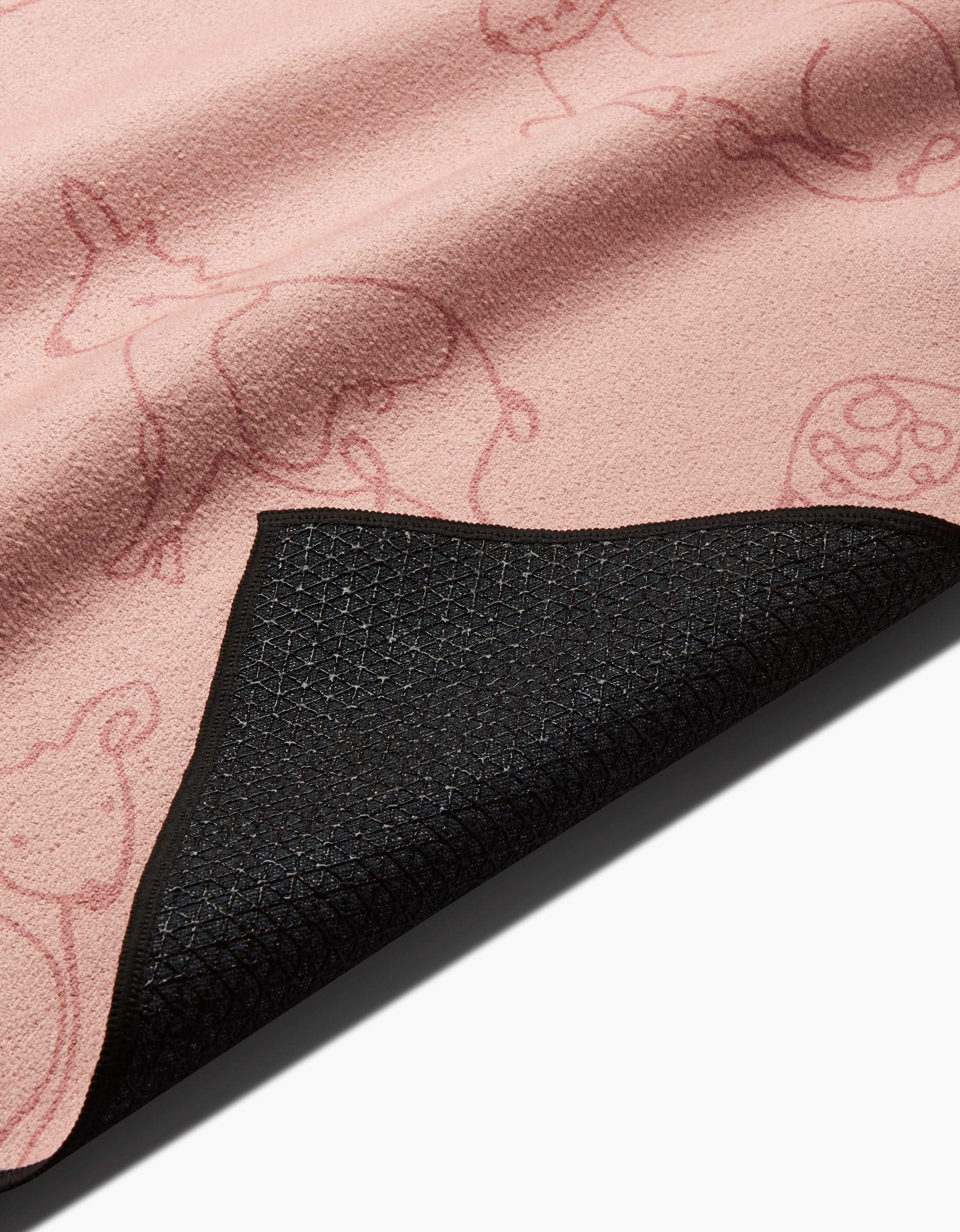 A close-up of Sara Mari’s Kidding Around yoga mat in pink, featuring faint animal outlines and a corner flipped to reveal its textured, black, slip-resistant underside.