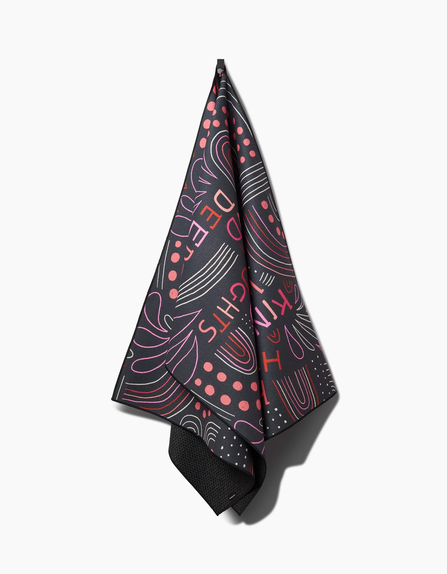 The Kind Hearts yoga towel by Jessica Swift features dark recycled fabric with abstract floral and dotted pink, red, and purple patterns, plus partial stylized text, shown hanging against a white background.