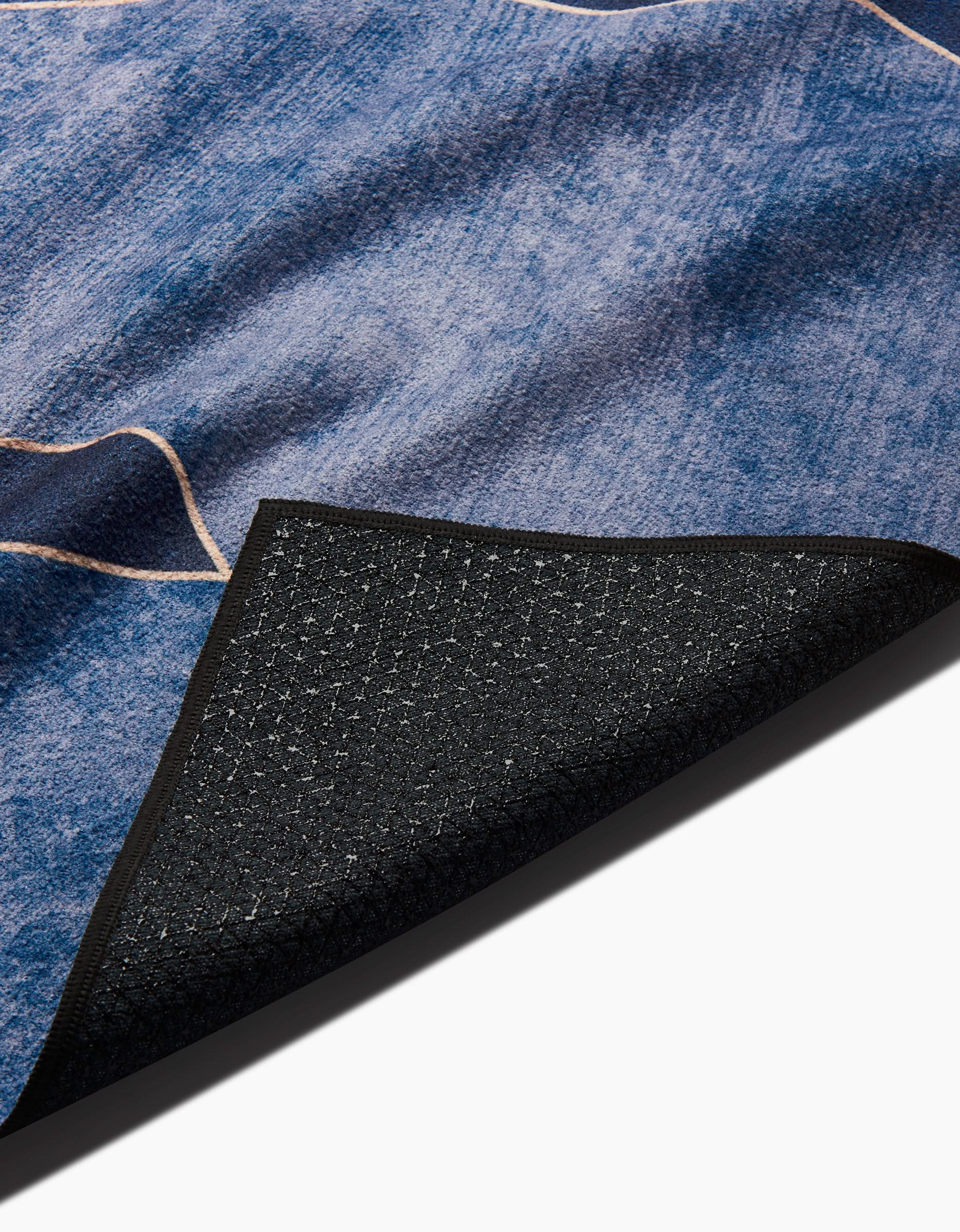 Close-up of the GEOMETRY Lined With Gold blue textured rug, corner flipped to reveal its dark, non-slip silicone grip backing and intricate underside pattern.