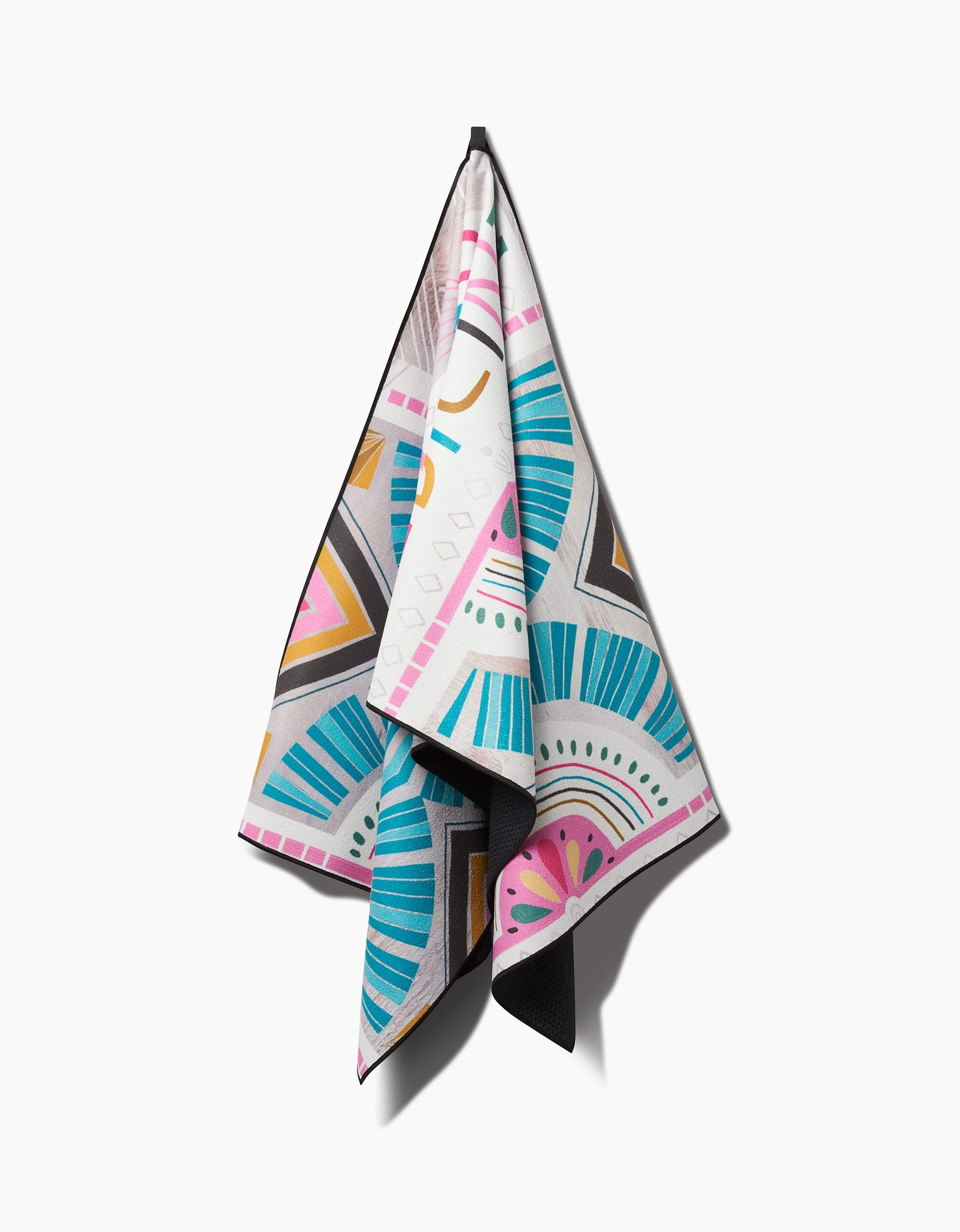 The Love is Good Medicine yoga towel by Jessica Swift, featuring vibrant geometric patterns in teal, pink, yellow, black, and white, hangs on a hook against a white background.