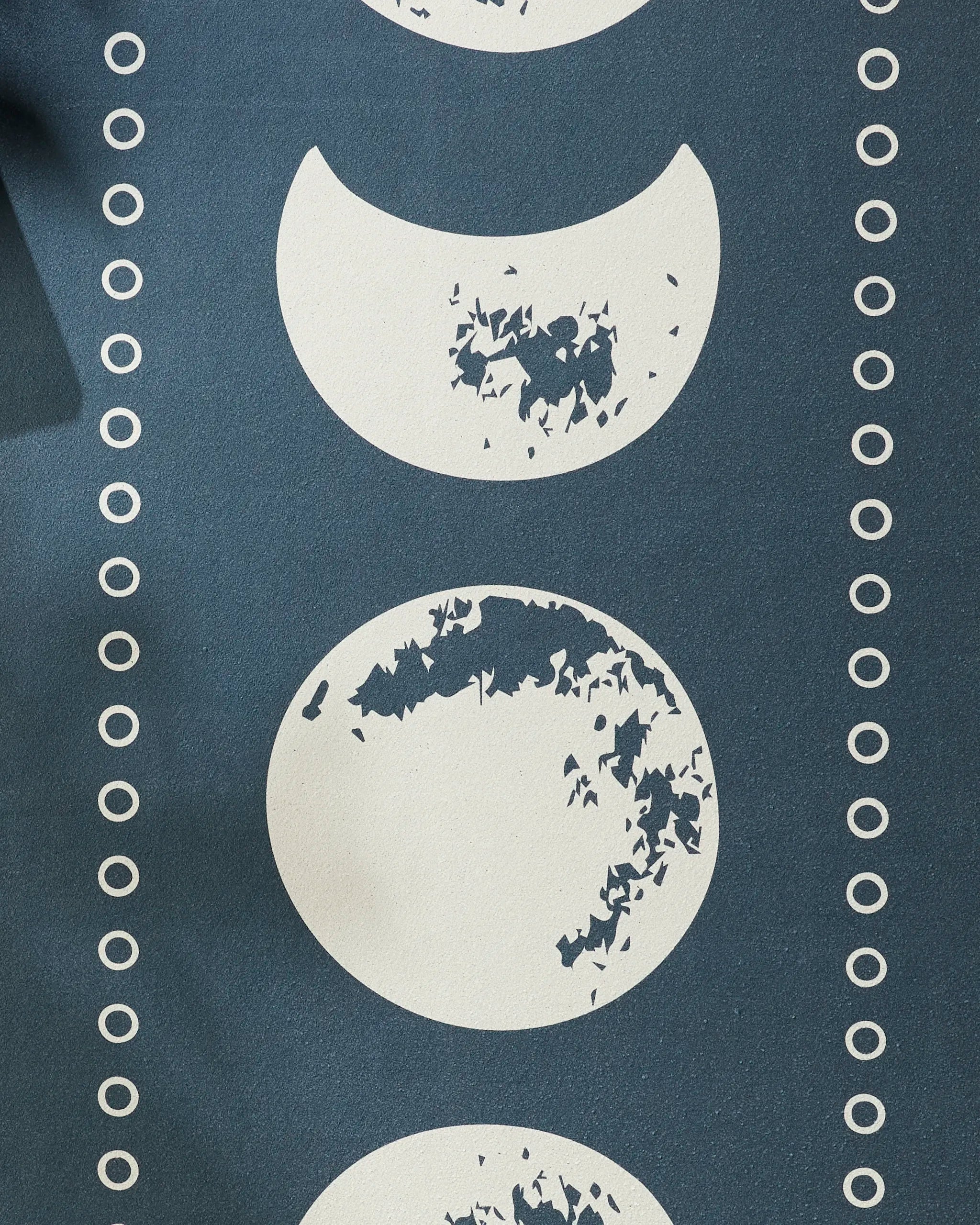 The Lunar Phases yoga towel by Ashley Celena features a blue background with vertically aligned white moon phases, crater-like textures, and columns of small white circles for both style and slip-resistance.
