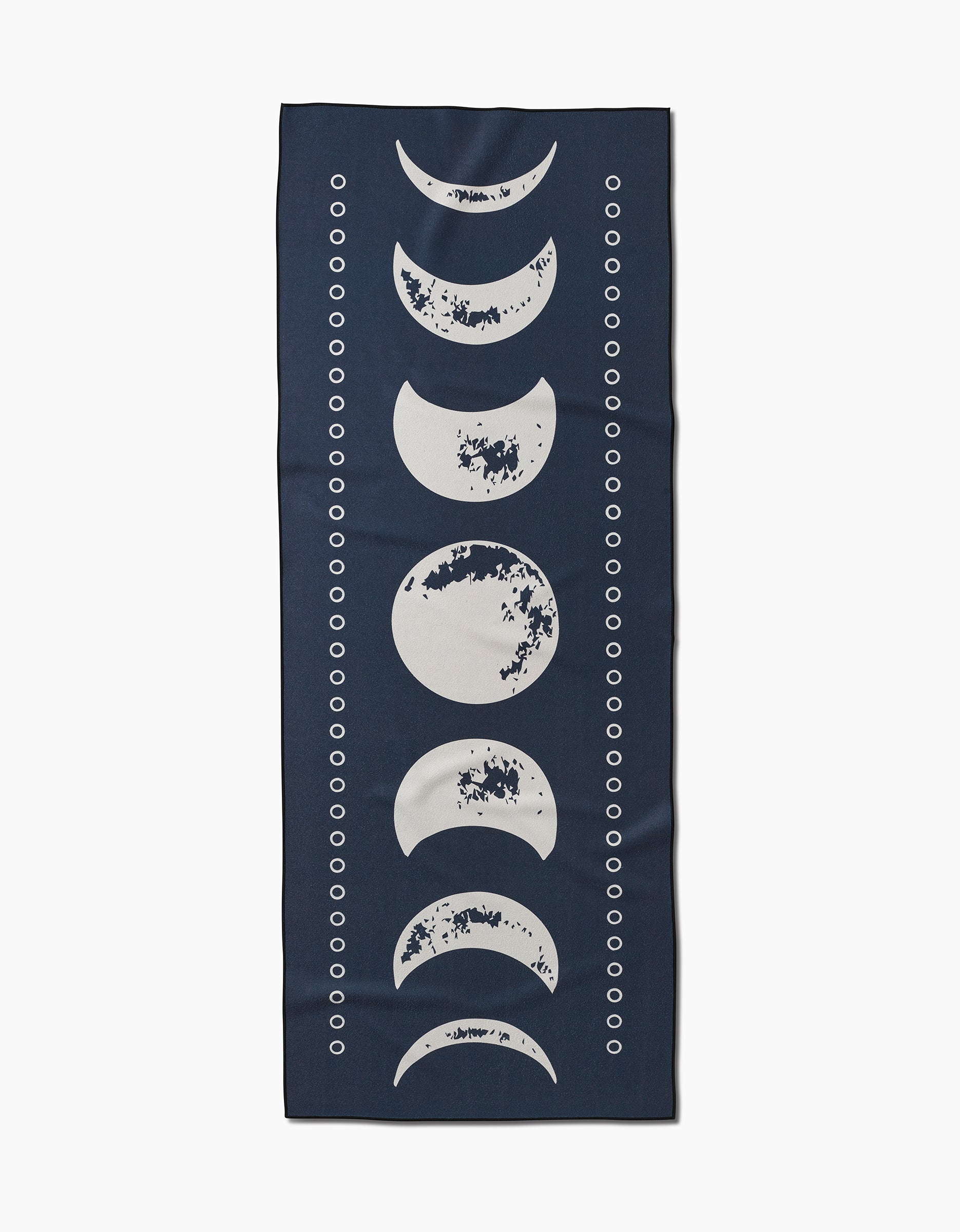 The Ashley Celena Lunar Phases is a dark blue rectangular yoga towel made from recycled materials, with white moon phases down the center and small white circles along both sides.