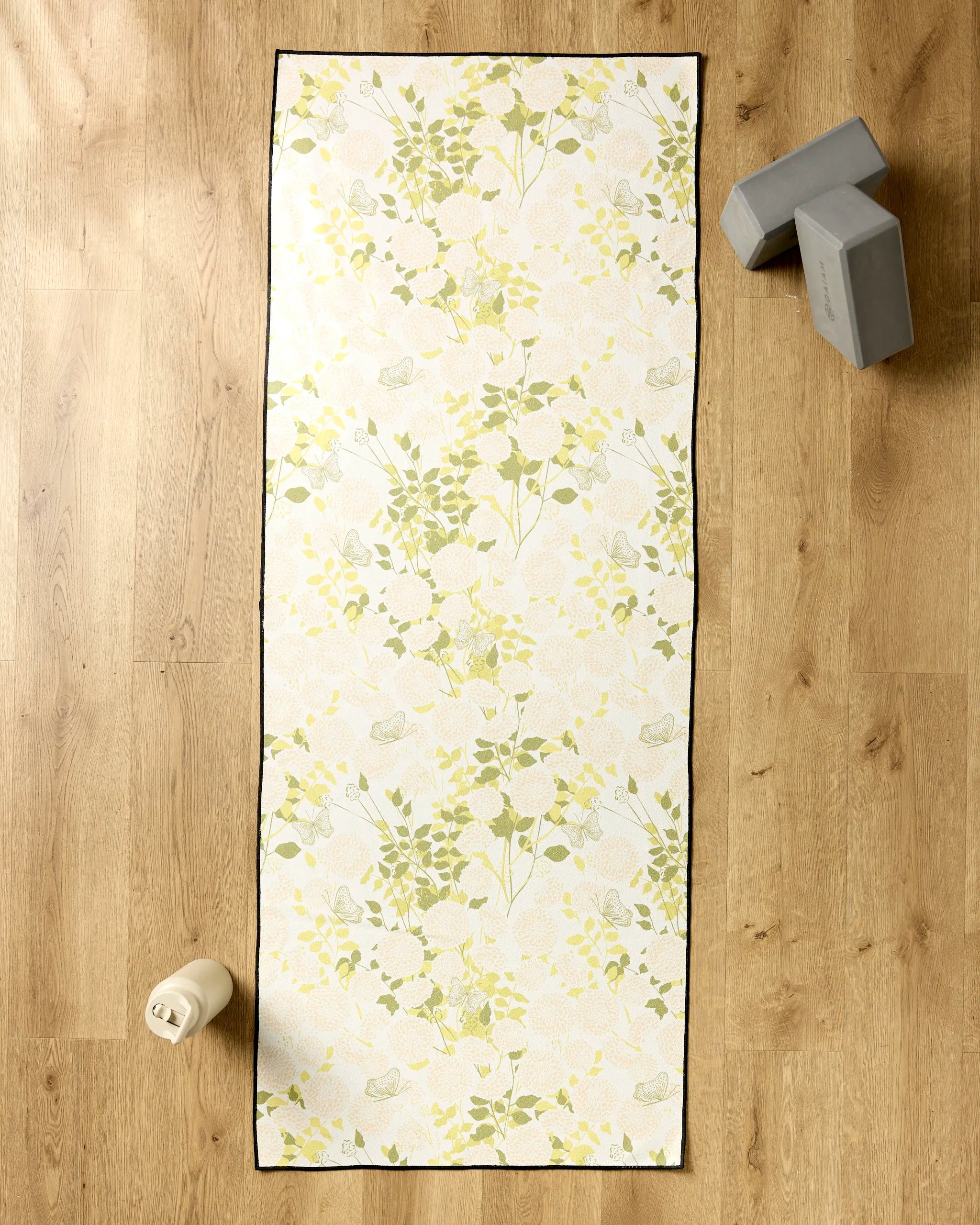 The Second Nature Studio Lush Garden yoga mat is laid out on a wooden floor, with gray yoga blocks, a beige water bottle, and a non-slip towel nearby for extra comfort during your practice.