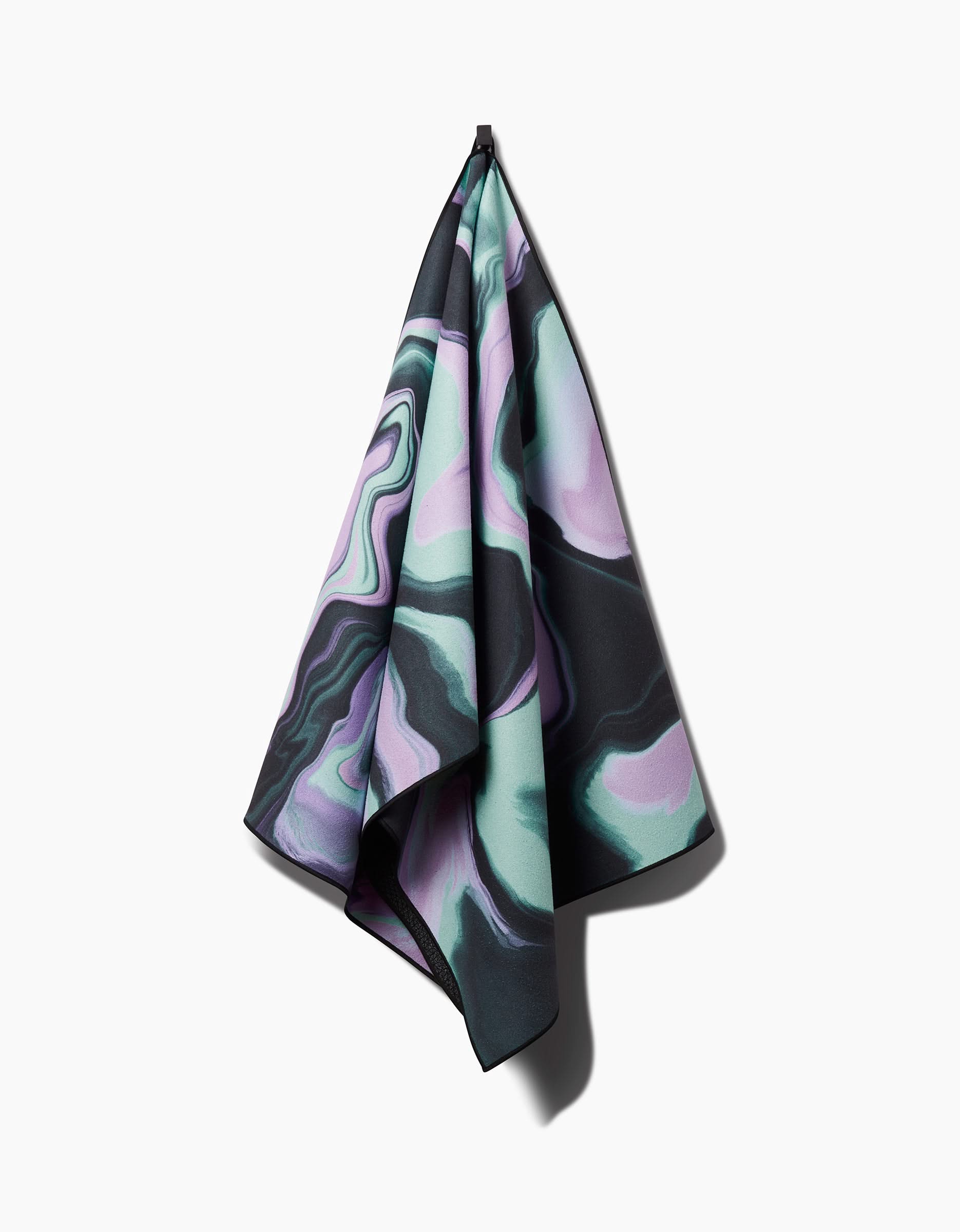The GEOMETRY Marble yoga towel, made from recycled materials and featuring a marbled pattern in pastel purple, green, and black, hangs from a hook against a white background.