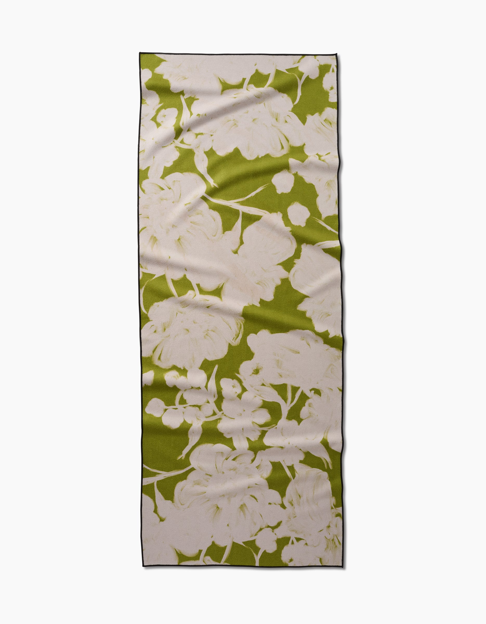 The GEOMETRY Meadow Mist yoga towel, rectangular and green with a bold white floral design, made from recycled materials, is shown flat with slight wrinkles on a white background.