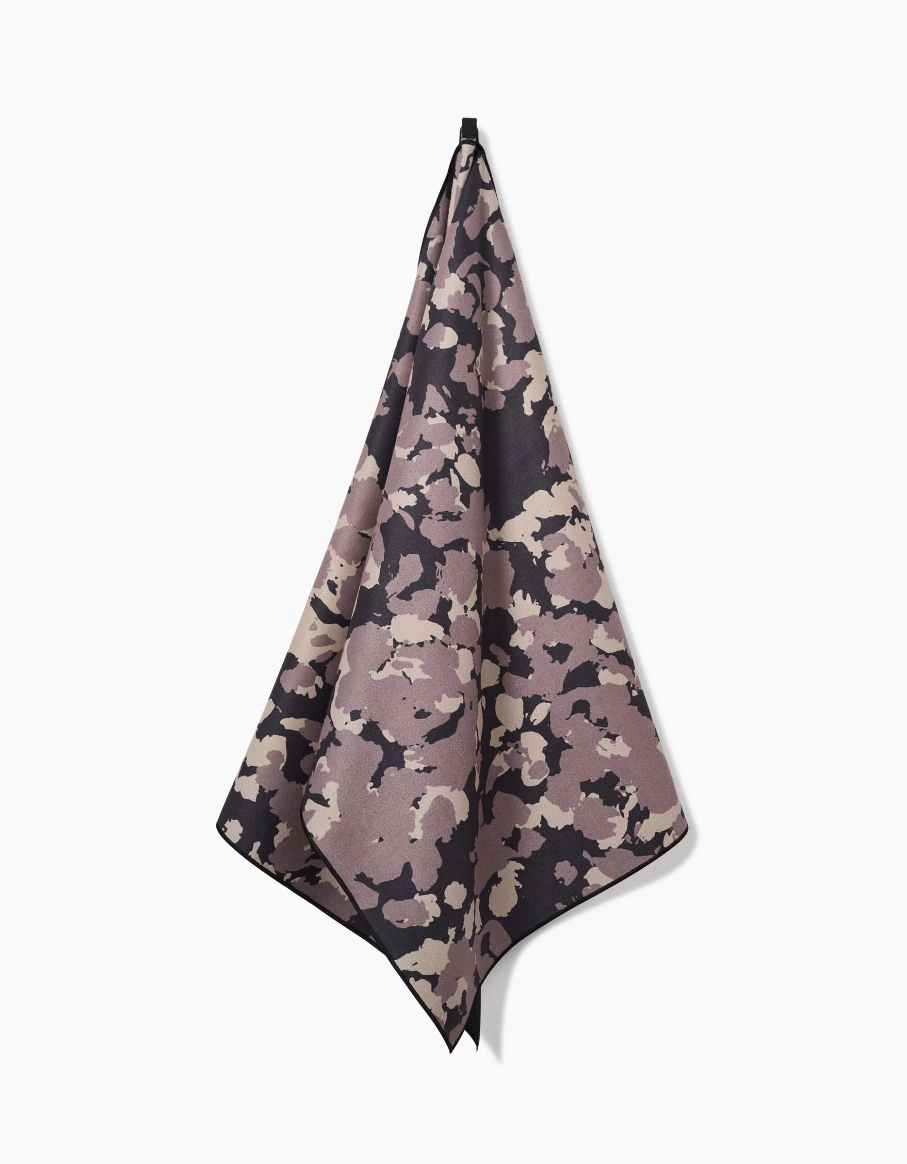 A GEOMETRY Metro Mesh yoga towel, crafted from recycled materials and showcasing a beige, black, and mauve camouflage pattern, hangs from a hook against a plain white background.