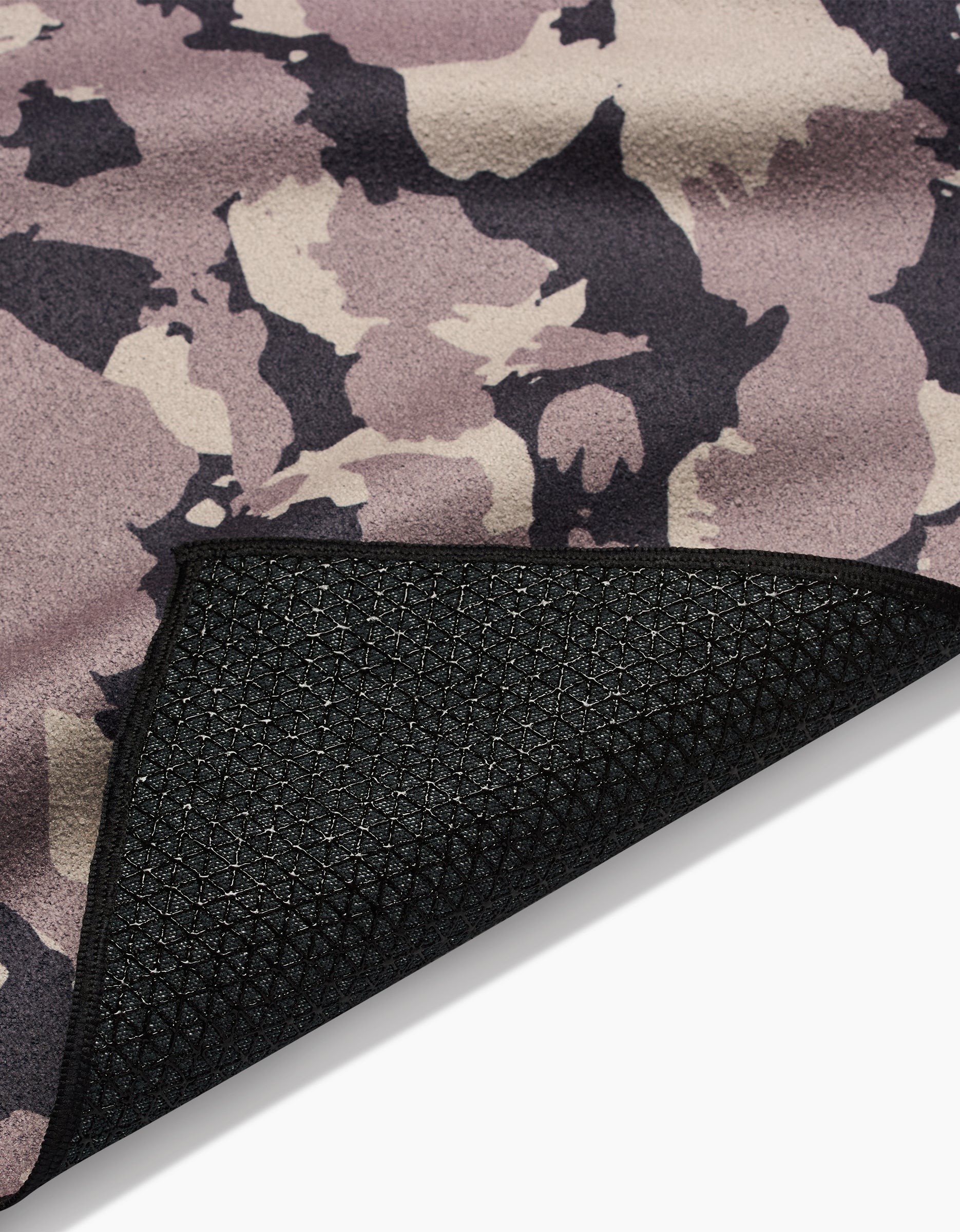 A close-up of the GEOMETRY Metro Mesh yoga towel in a purple, beige, and black camo pattern, featuring a flipped corner that reveals its textured black underside with geometric silicone grips for enhanced stability.