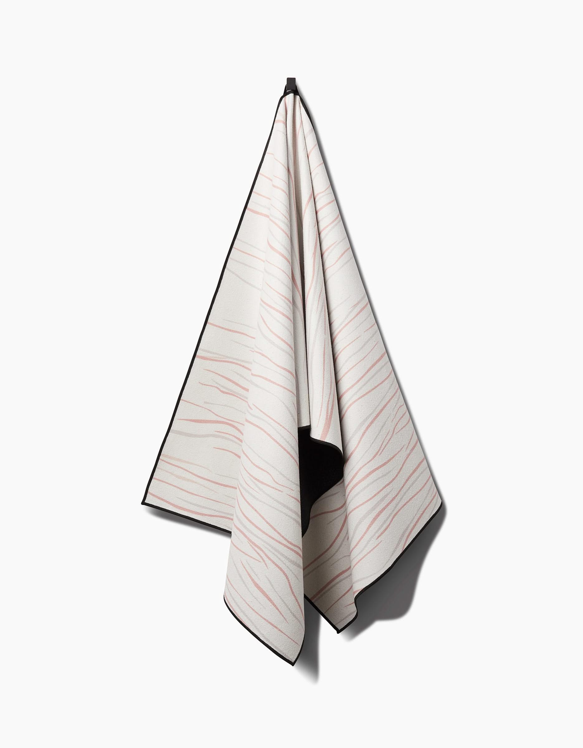 The GEOMETRY Mind yoga towel, crafted from recycled materials with thin wavy pink lines and black edging, is slip-resistant and hangs on a hook against a plain white background.