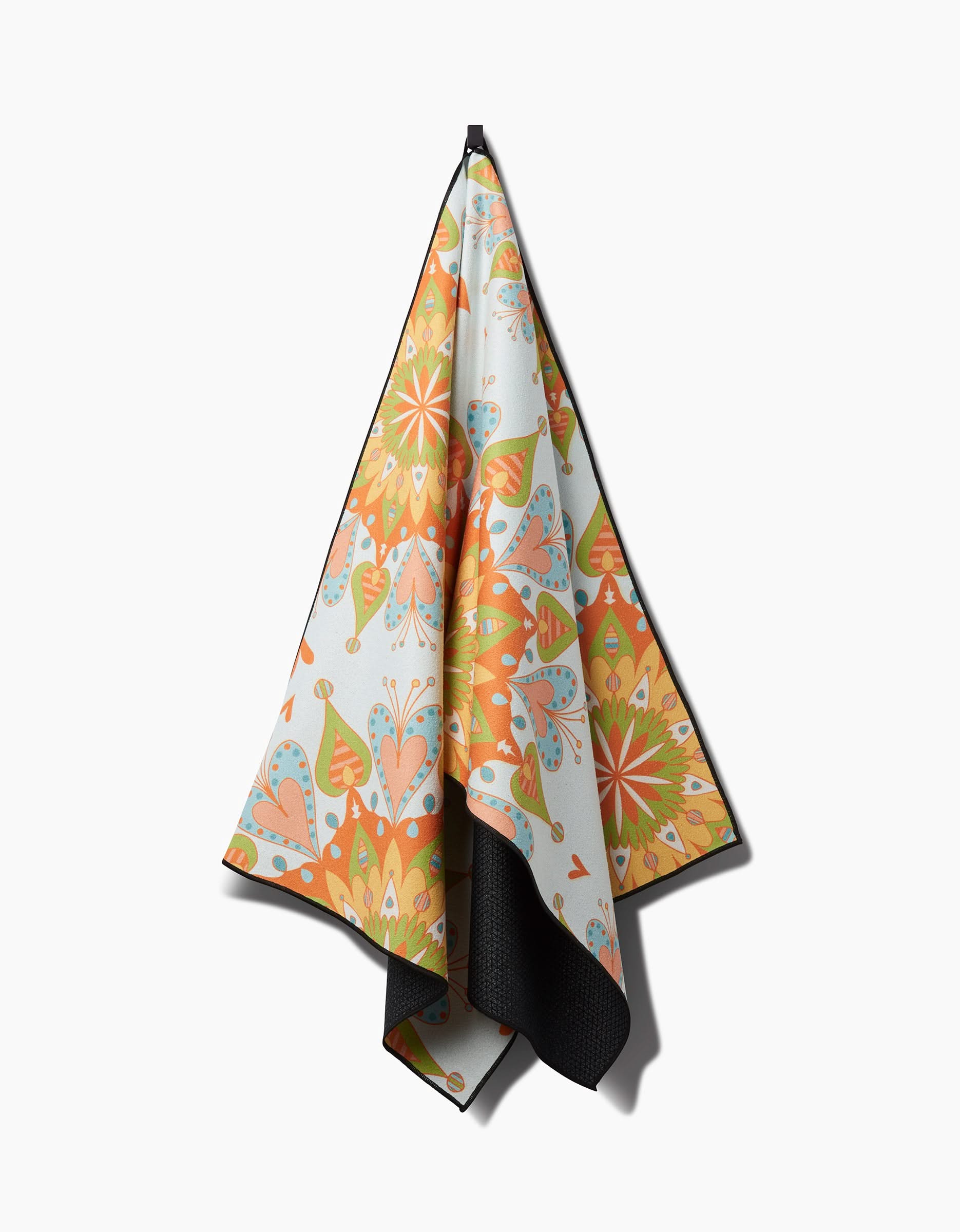 The Mindfulnice Mindful Mandalas recycled yoga towel, featuring an intricate floral and geometric pattern in orange, yellow, green, and blue, hangs on a hook against a white background.