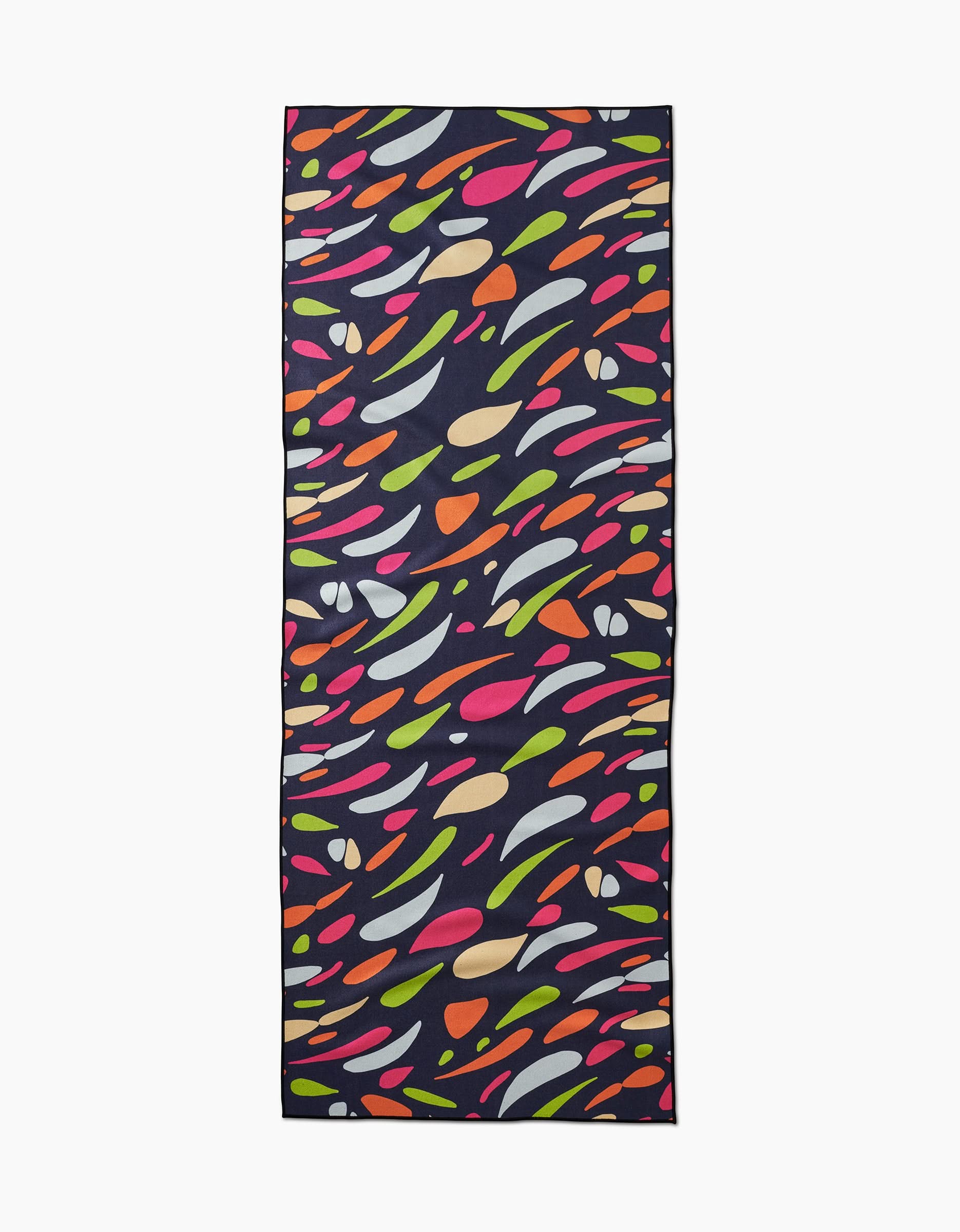 The GEOMETRY Motion yoga towel features a dark background with a colorful abstract pattern of curved shapes in pink, green, orange, yellow, white, and red, and is crafted from recycled materials.