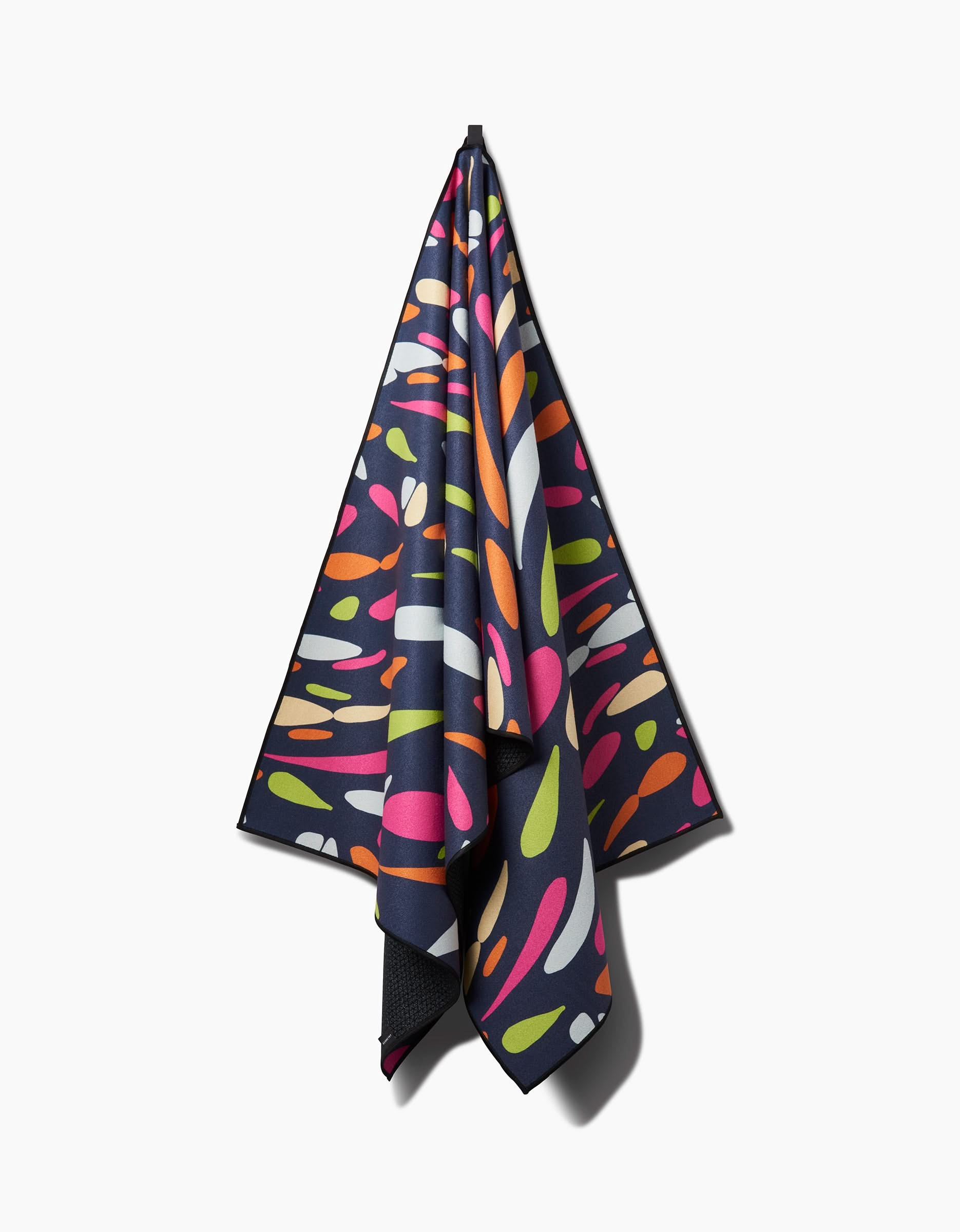 The GEOMETRY Motion yoga towel, dark-colored with a slip-resistant surface, showcases colorful irregular shapes in pink, orange, green, white, and red and is displayed against a plain white background.